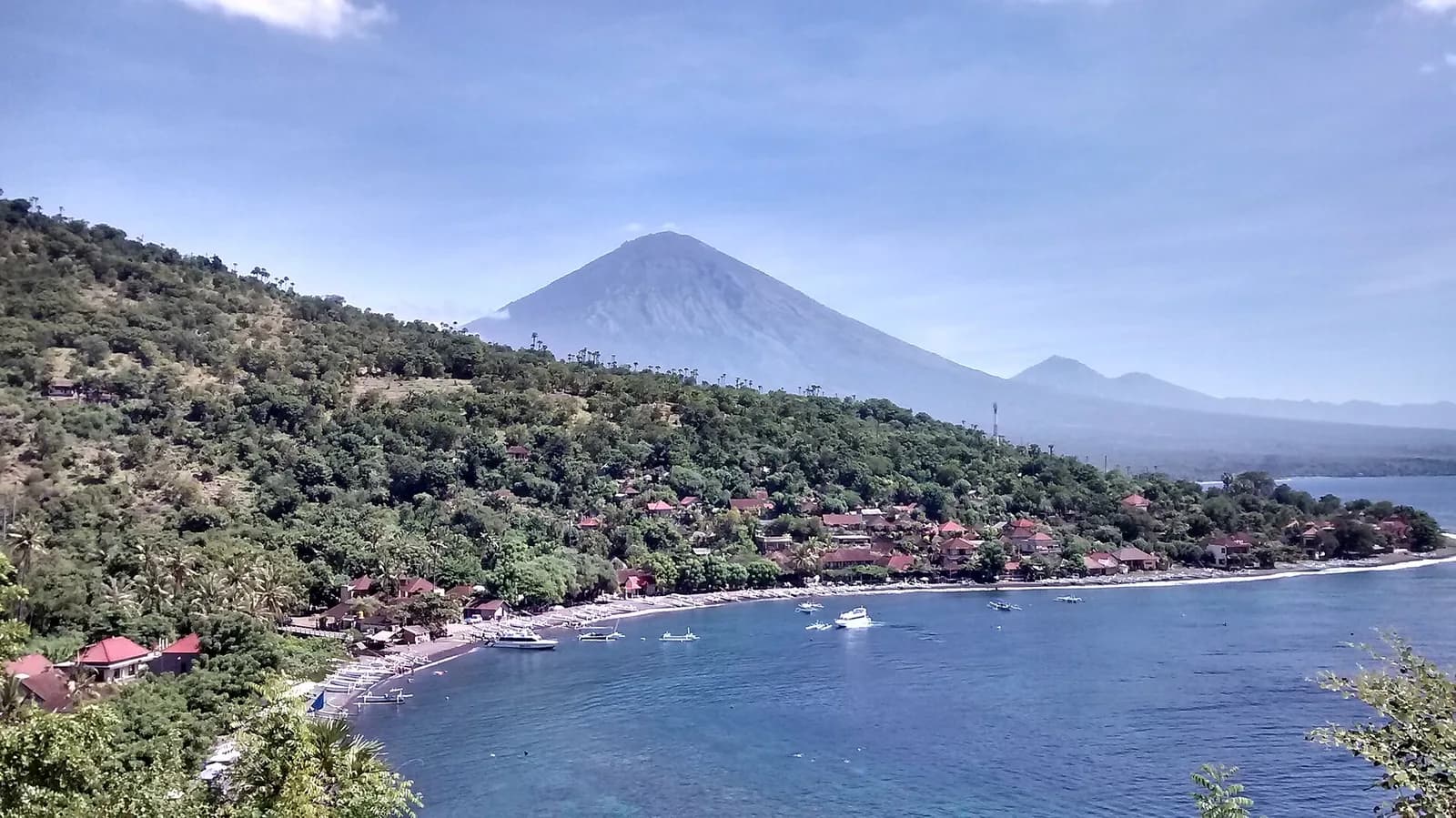 Jemeluk Bay seen from the clifftop viewpoint in Amed, with dive boats moored offshore and Mount Agung in the background, Bali