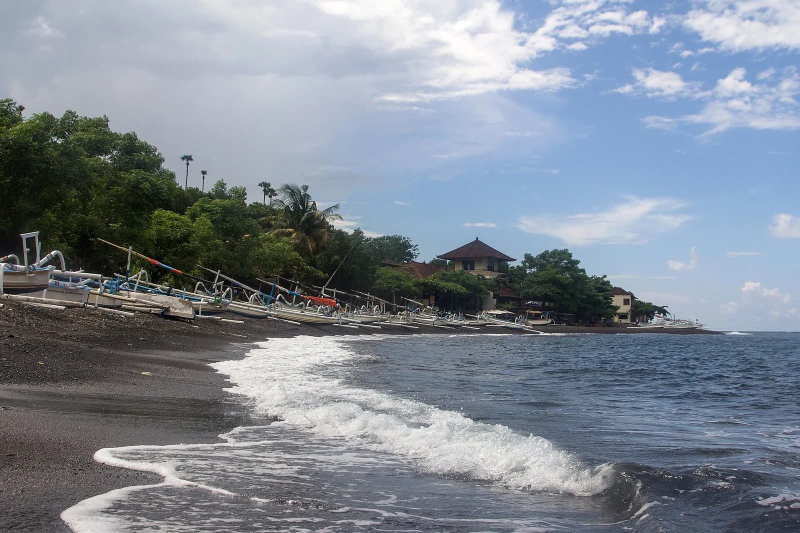 Row of white jukung outrigger boats lined up on the black volcanic sand of Amed beach, east Bali