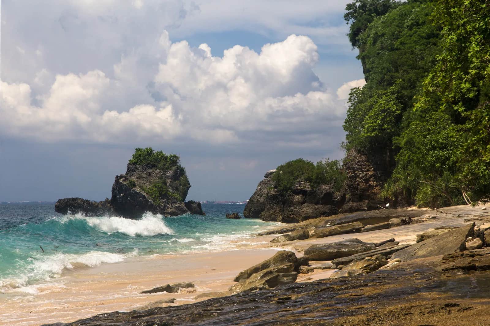 The rock stack and green headland at Padang Padang Beach with a wave breaking on the reef, Uluwatu, Bali