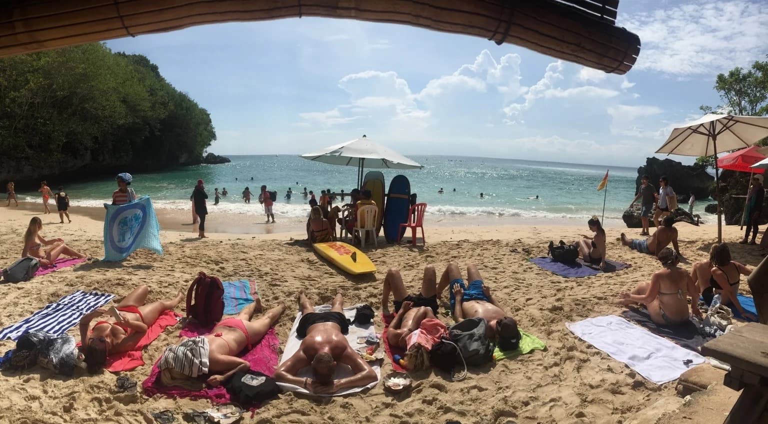 Padang Padang Beach at midday, towels and sunbathers covering the sand with swimmers in the cove, Uluwatu, Bali