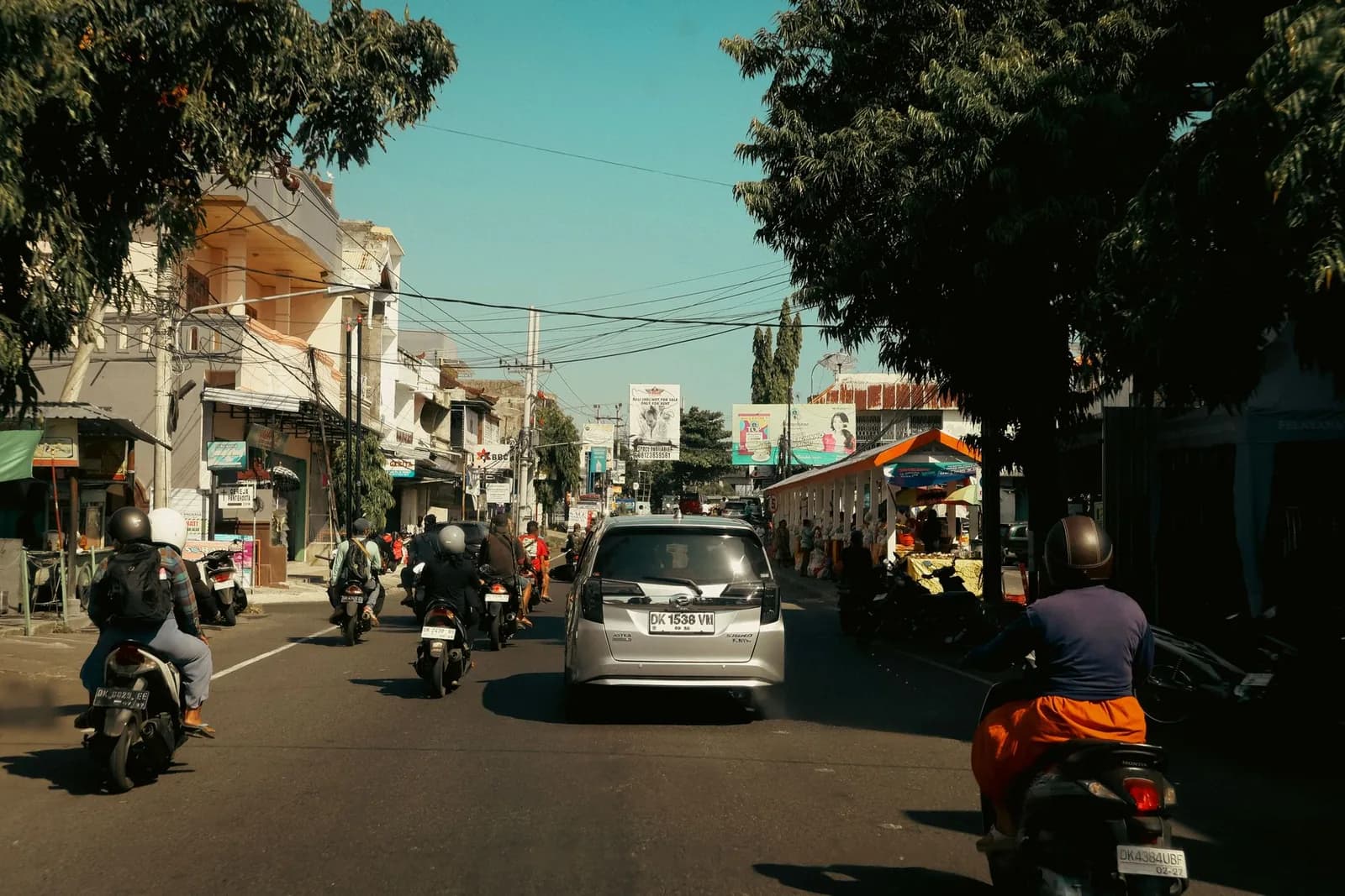 Scooters and cars sharing a busy main road lined with shops and warungs in Bali