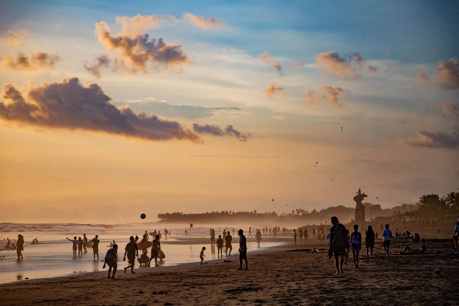 Crowds on the grey volcanic sand of Canggu beach at sunset, Bali, with a red warning flag at the waterline