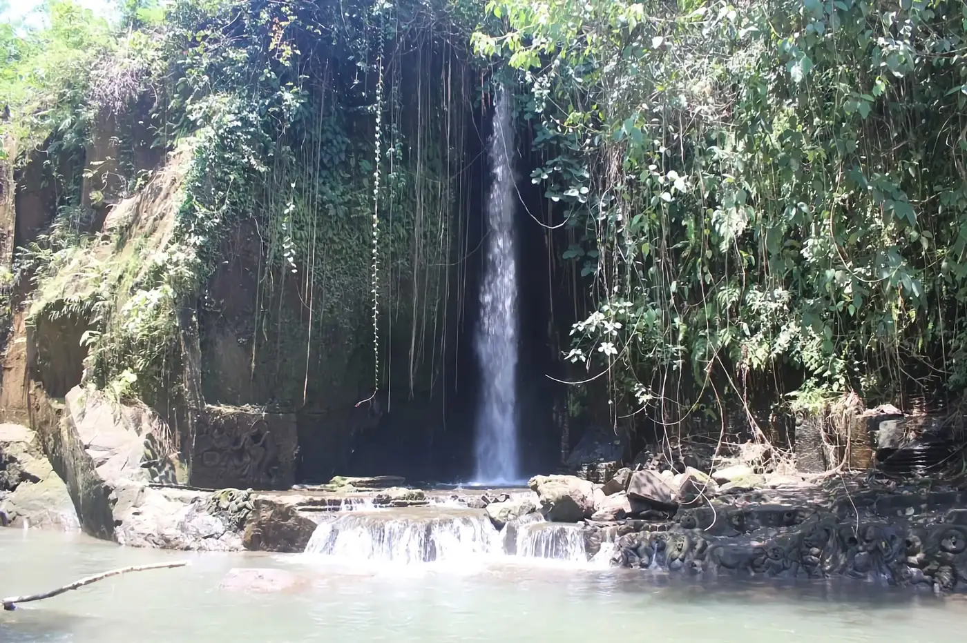 Sumampan waterfall in Gianyar, a narrow fall over a carved stone wall into a green pool