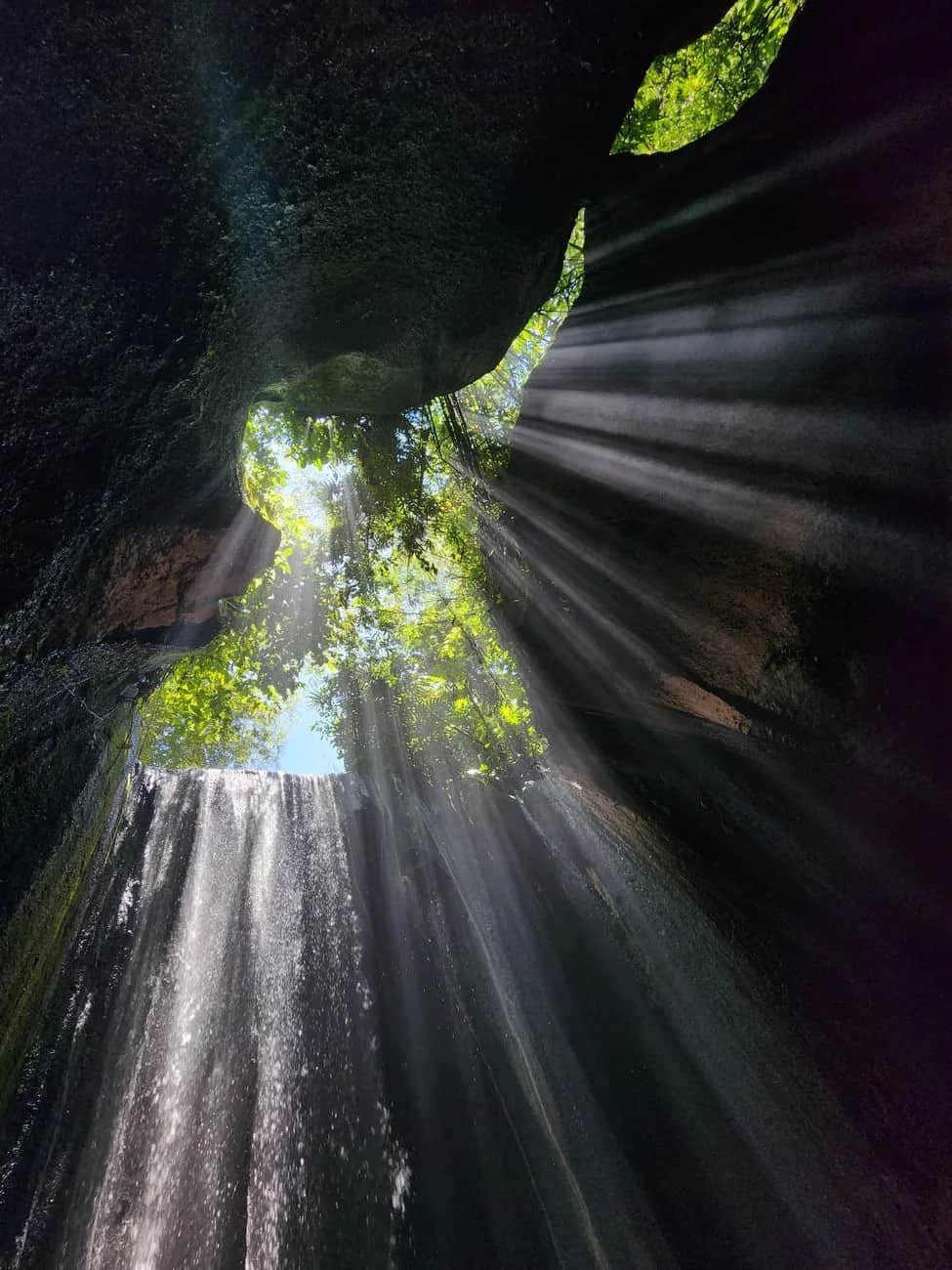 Shafts of sunlight falling through the canyon opening onto the water at Tukad Cepung, Bali