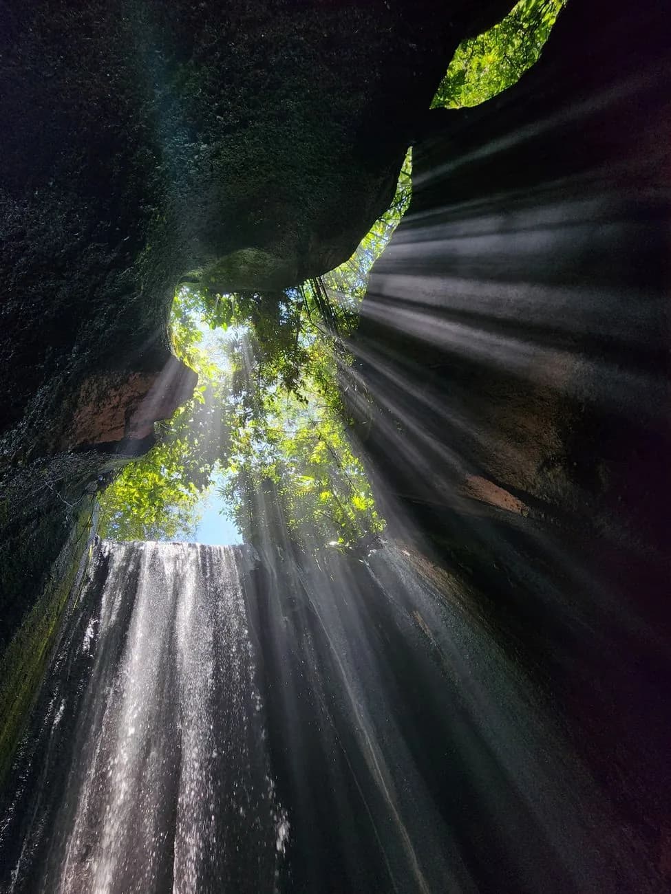 Shafts of light falling through the open roof of the gorge onto the water at Tukad Cepung
