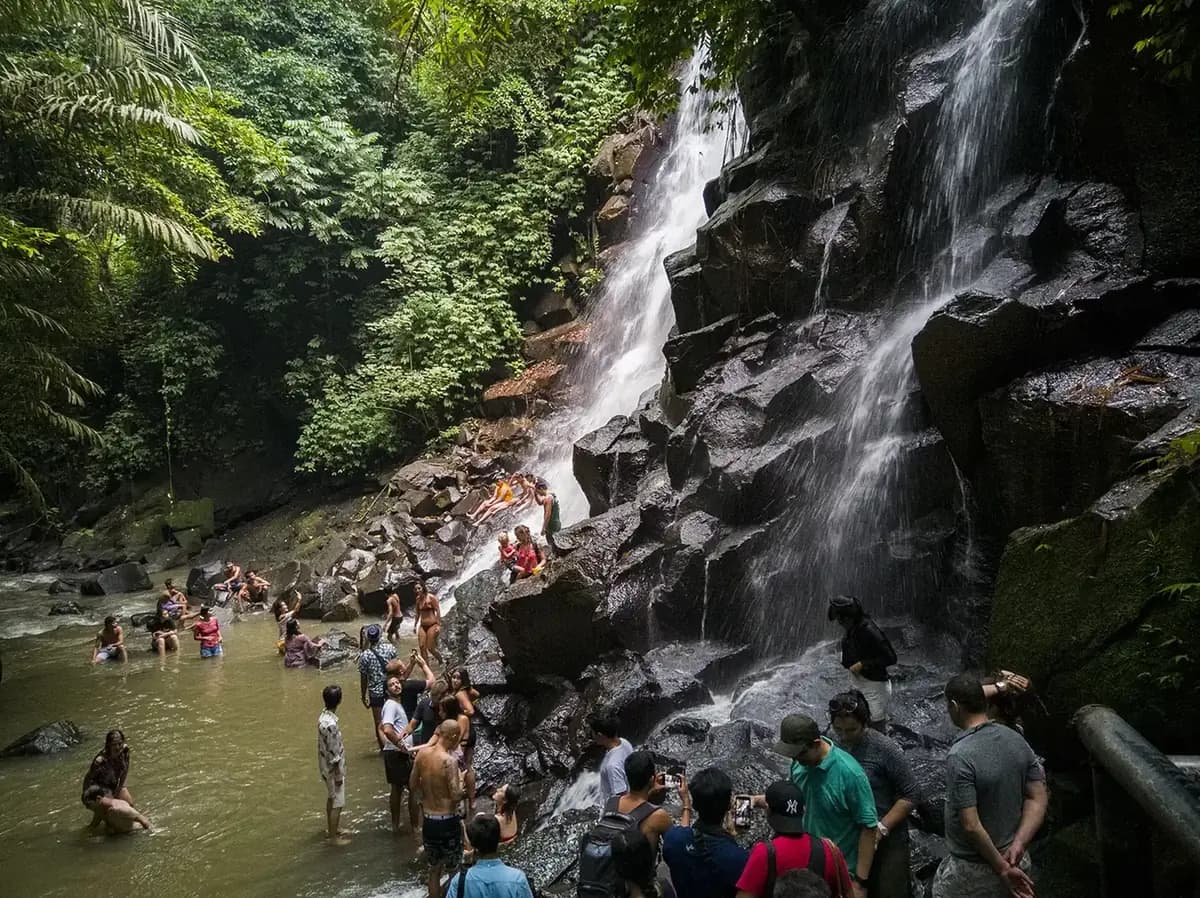 Crowds of visitors photographing Kanto Lampo waterfall from the shallow brown pool at its base