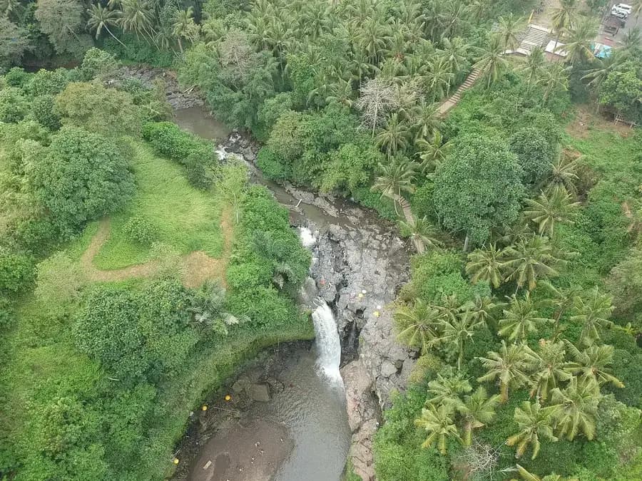 Aerial view of the Tegenungan river cutting through coconut groves and farmland, with the car park and staircase visible