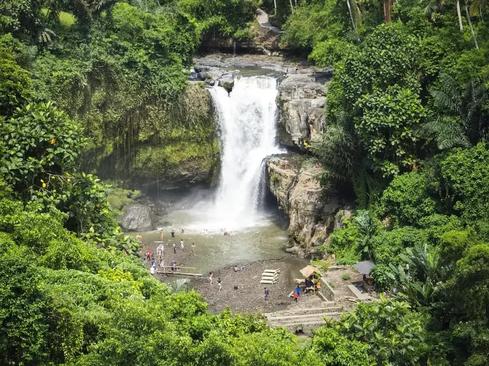 Tegenungan waterfall seen from the upper viewpoint, with visitors on the gravel bank below