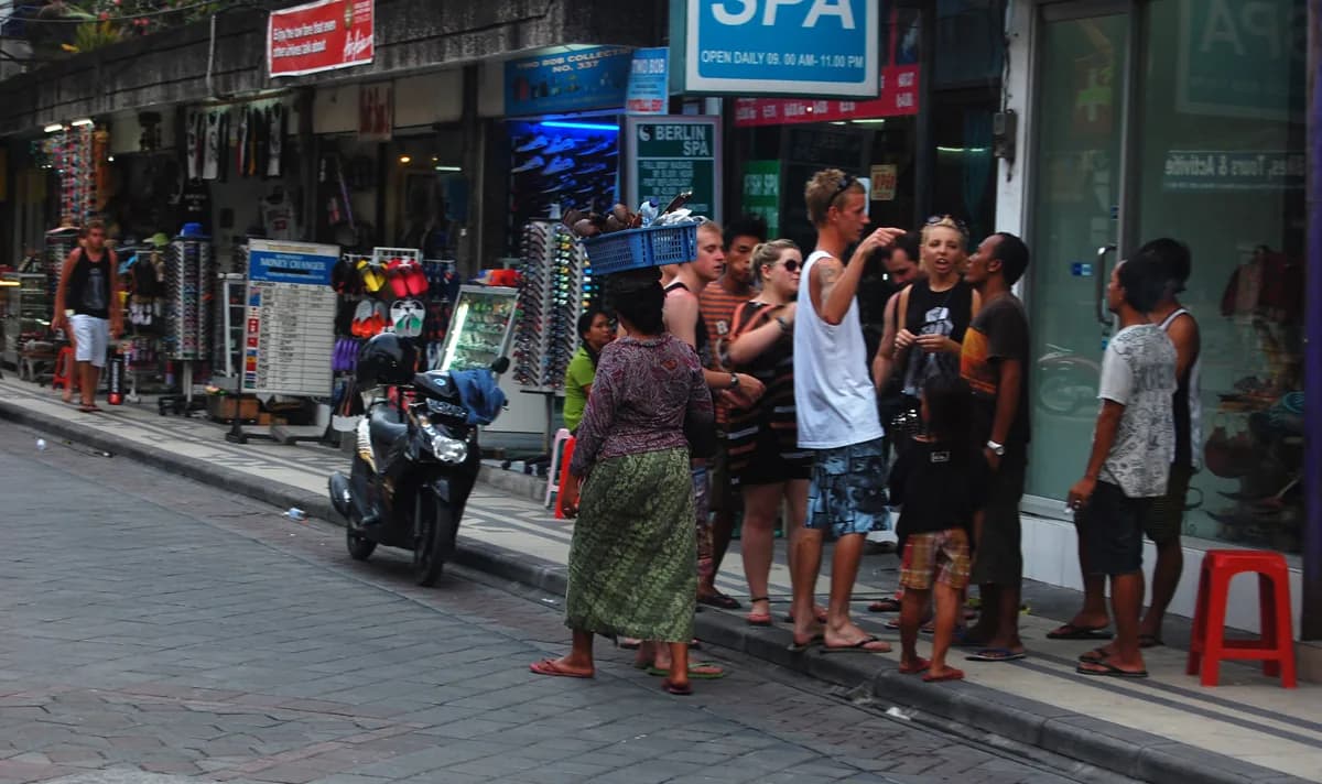 Daytime view of Jalan Legian in Kuta, Bali, with souvenir shops, a parked scooter and tourists on the pavement