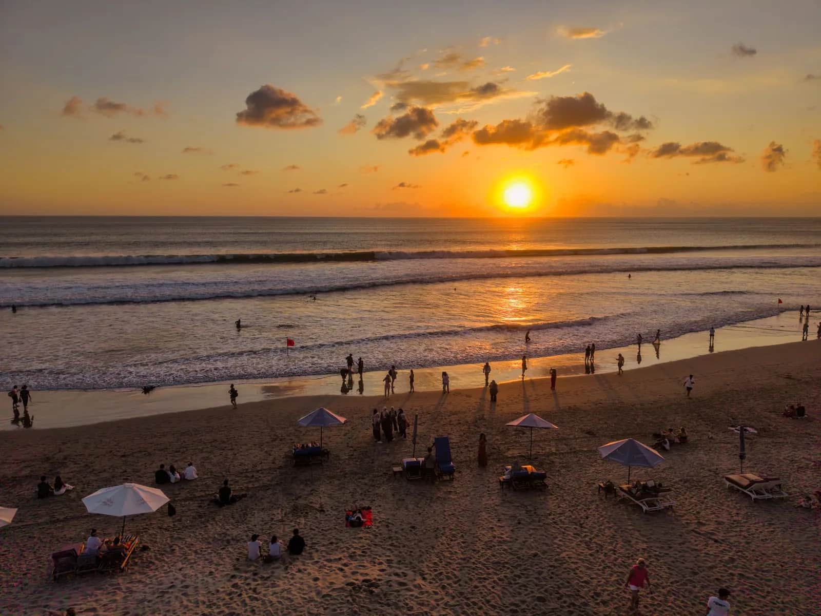 Sunset over Kuta Beach in Bali, with visitors on the wide sand beach and waves rolling in
