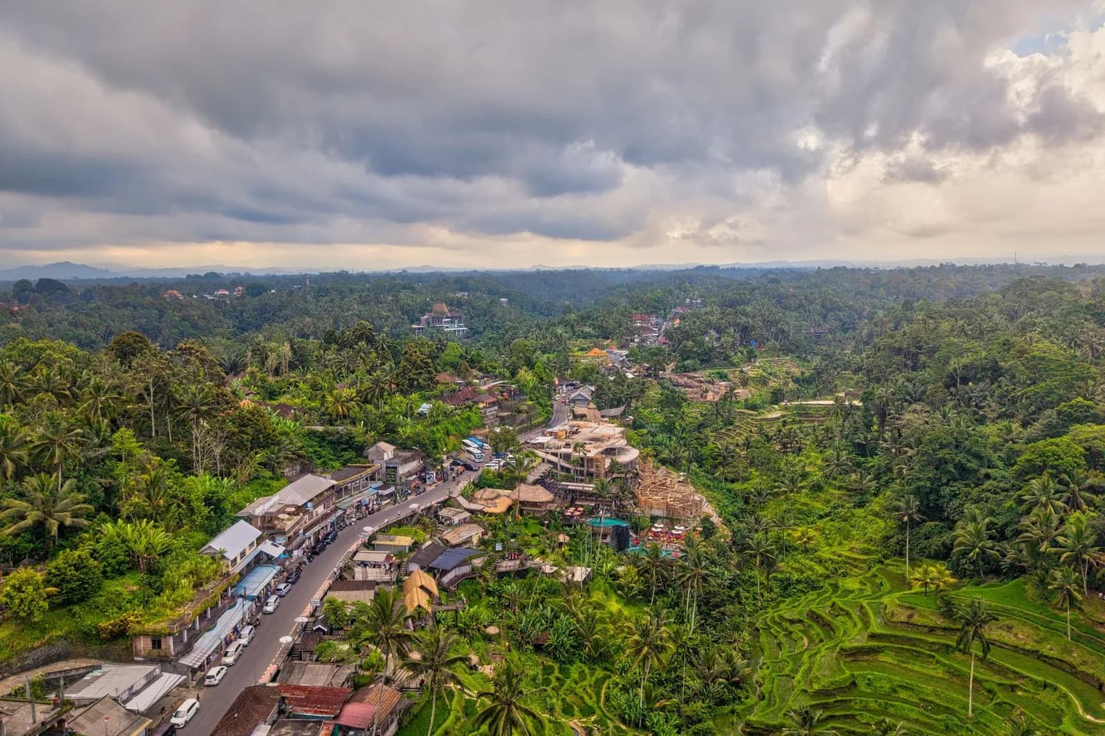 Dark monsoon storm clouds building over terraced rice fields and a café-lined road in the Bali highlands