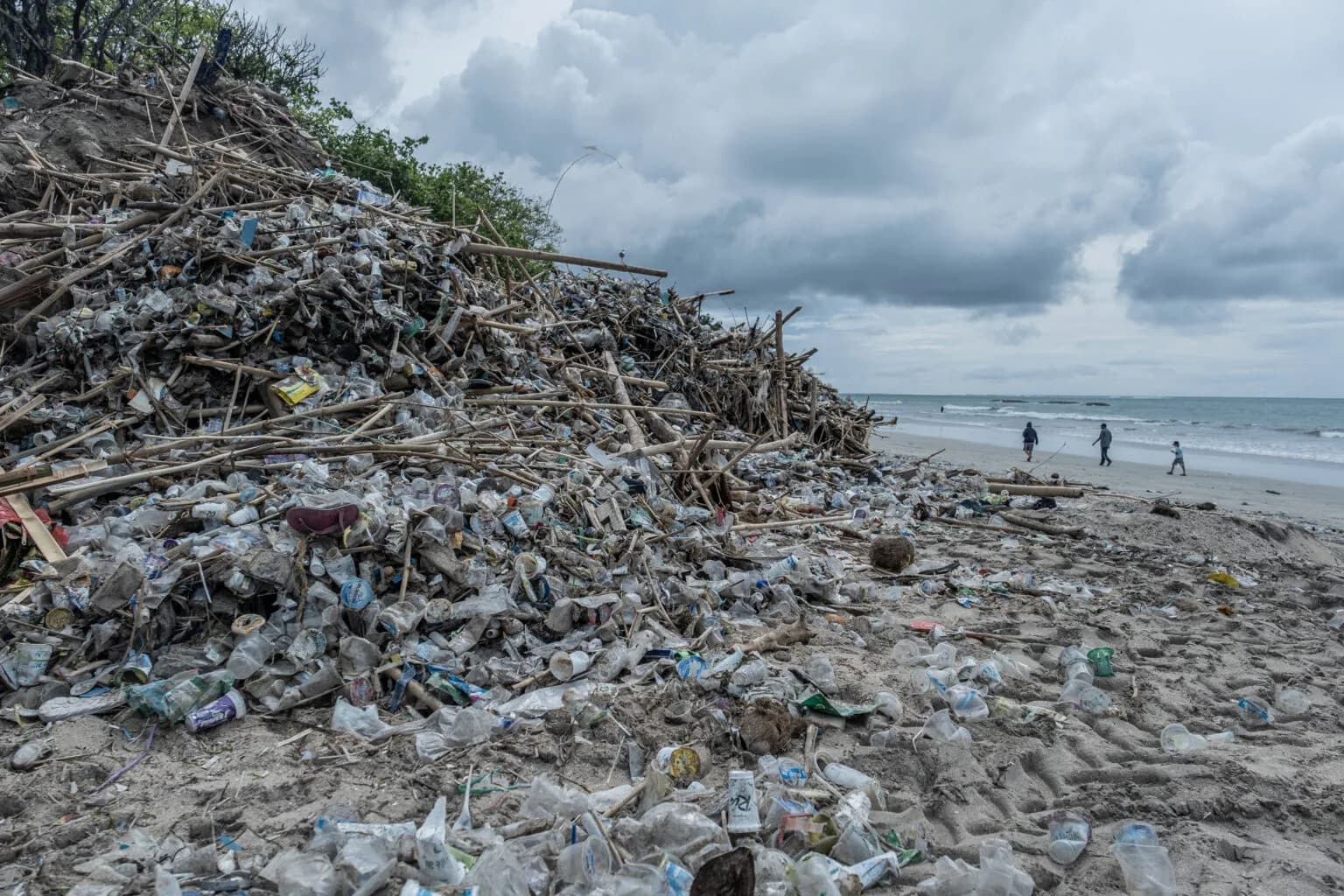 Plastic bottles and bamboo debris washed up on Kuta Beach in Bali under a stormy sky in January