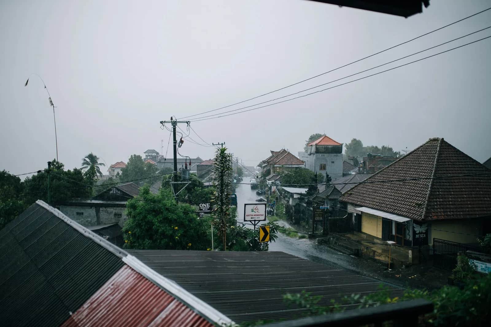 Rain falling over the tiled roofs and temple gates of a Balinese village street in the wet season
