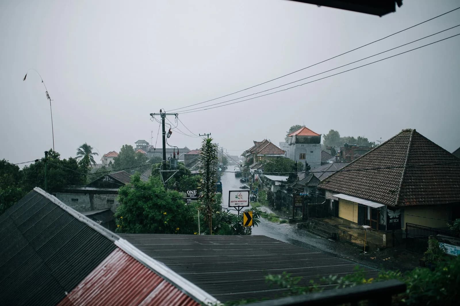 Rain falling over the tiled roofs and temple gates of a Balinese village street in the wet season