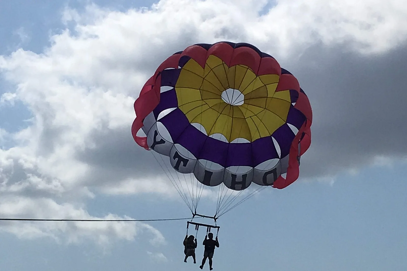 Two people parasailing under a colourful parachute above Tanjung Benoa, Bali