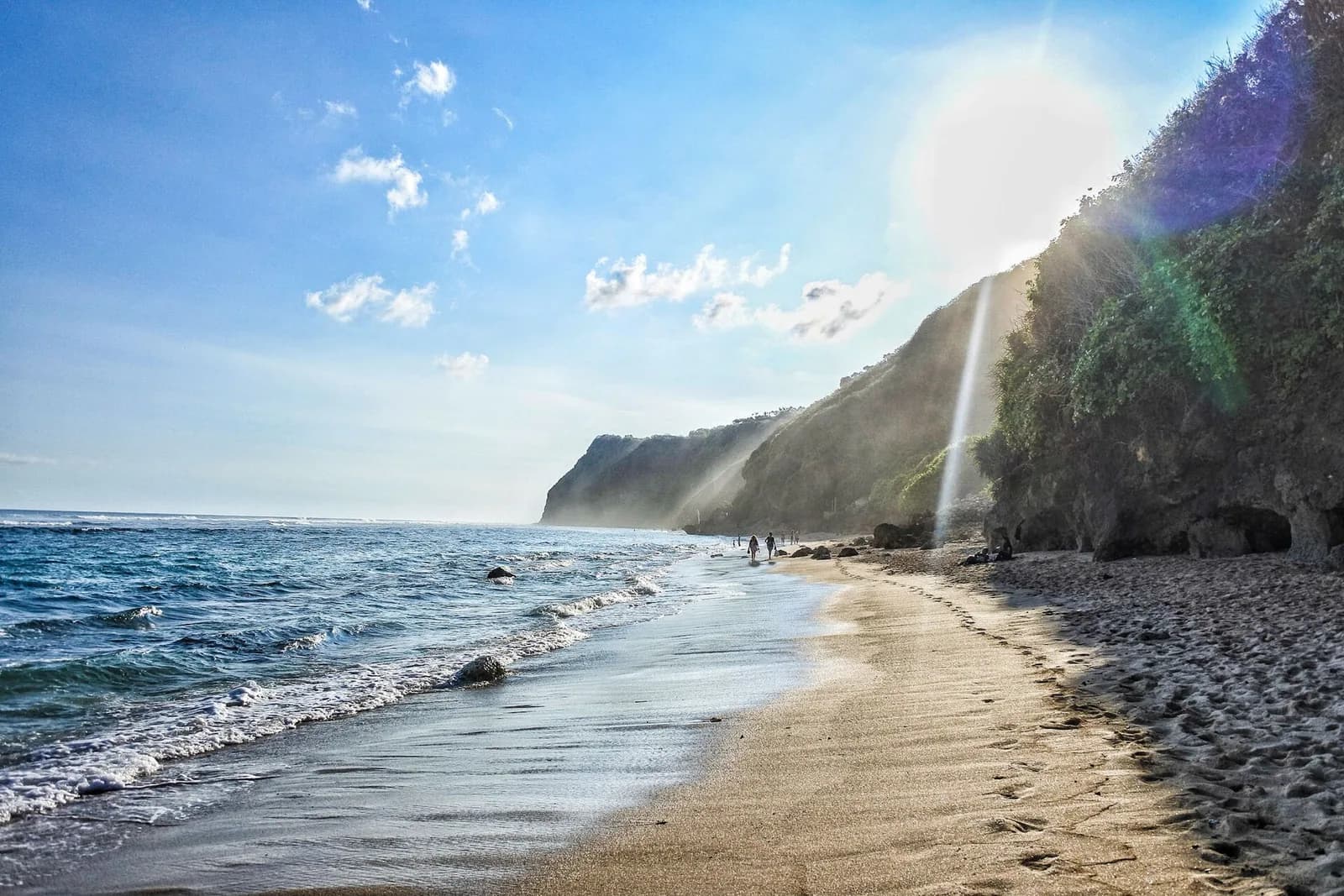 Mengiat Beach in Nusa Dua, Bali, with small waves rolling onto a sandy shore below low limestone cliffs
