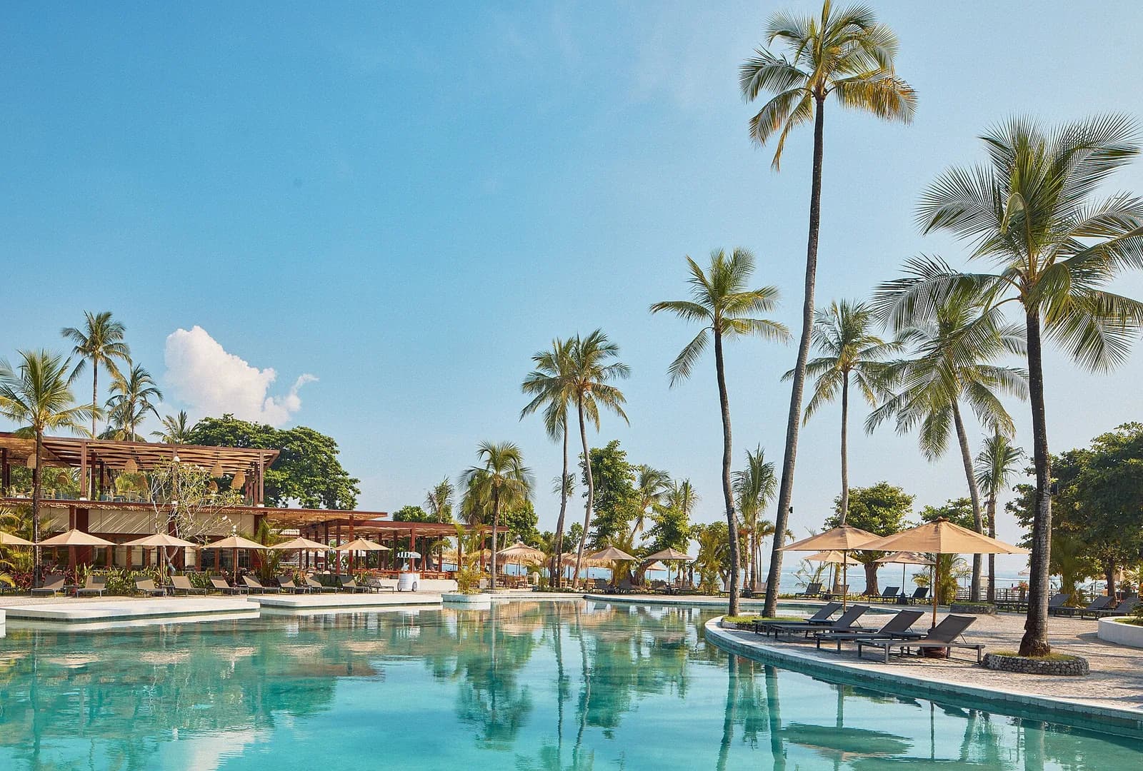 Resort swimming pool framed by tall coconut palms and beach pavilions at a Nusa Dua hotel, Bali