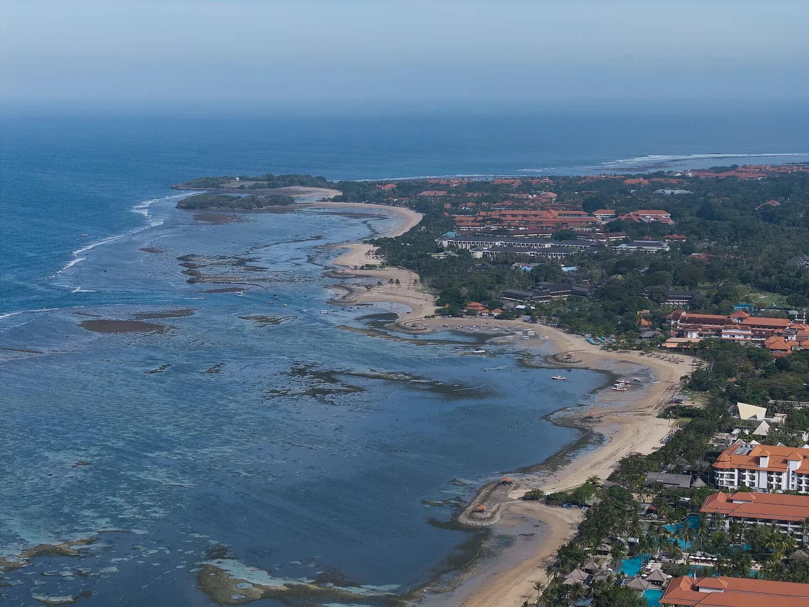 Aerial view of the Nusa Dua resort enclave on Bali's east coast, with beachfront hotels, sandy shoreline and the offshore reef