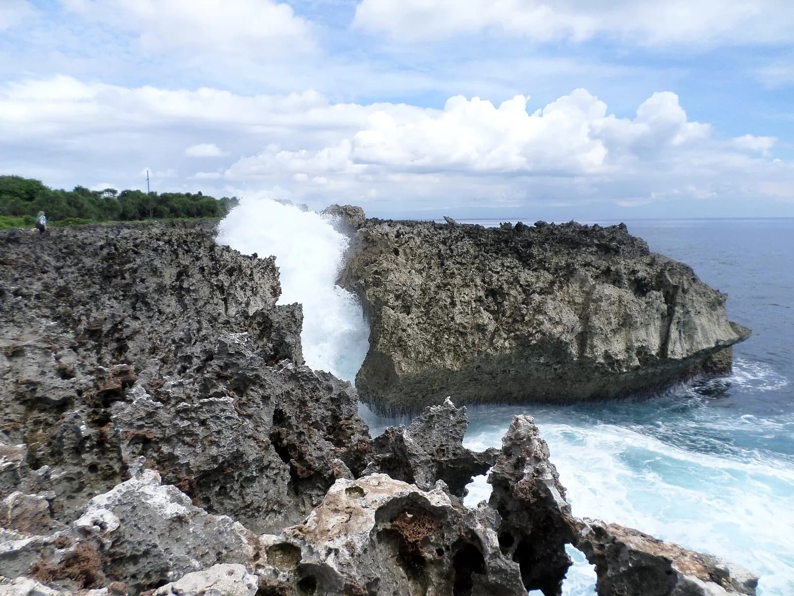 A wave surging up through a gap between jagged limestone rocks at the Water Blow, Nusa Dua, Bali