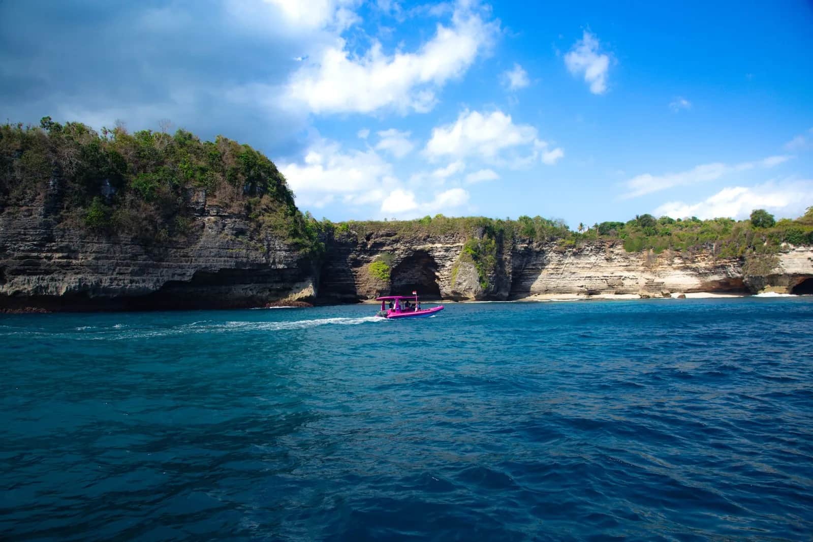 Small tour boat running below the eroded limestone cliffs of the Nusa Penida coast, Bali