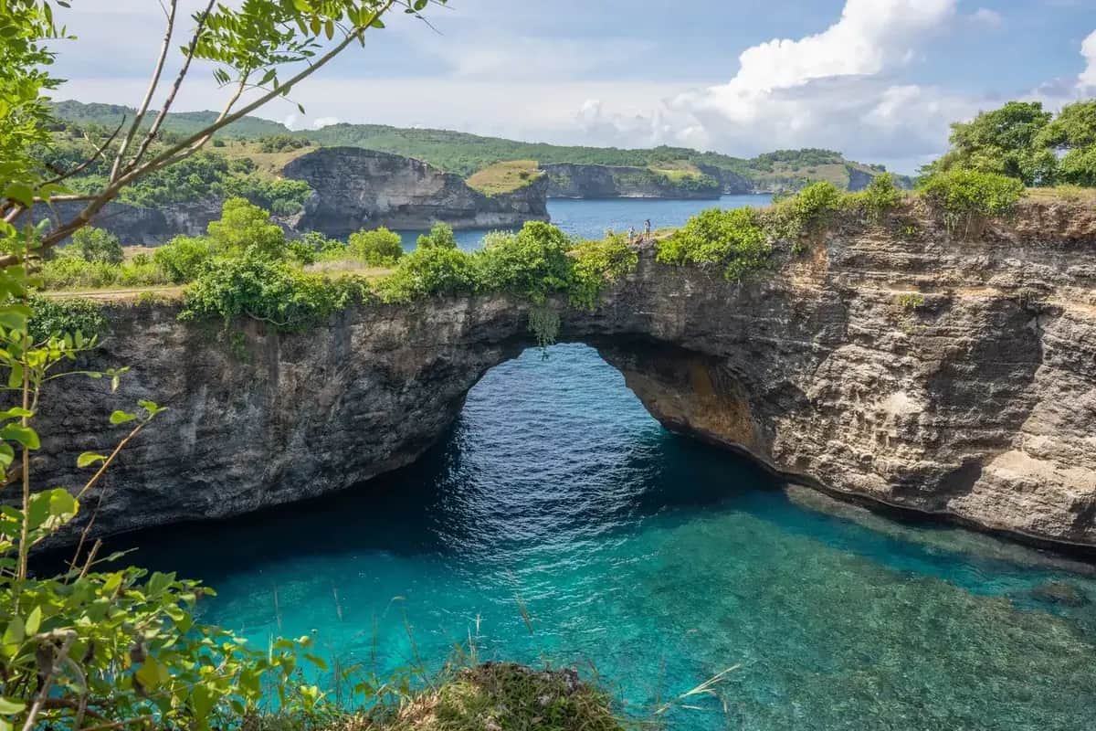 The natural arch of Broken Beach over its circular cove, with visitors on the clifftop path, Nusa Penida