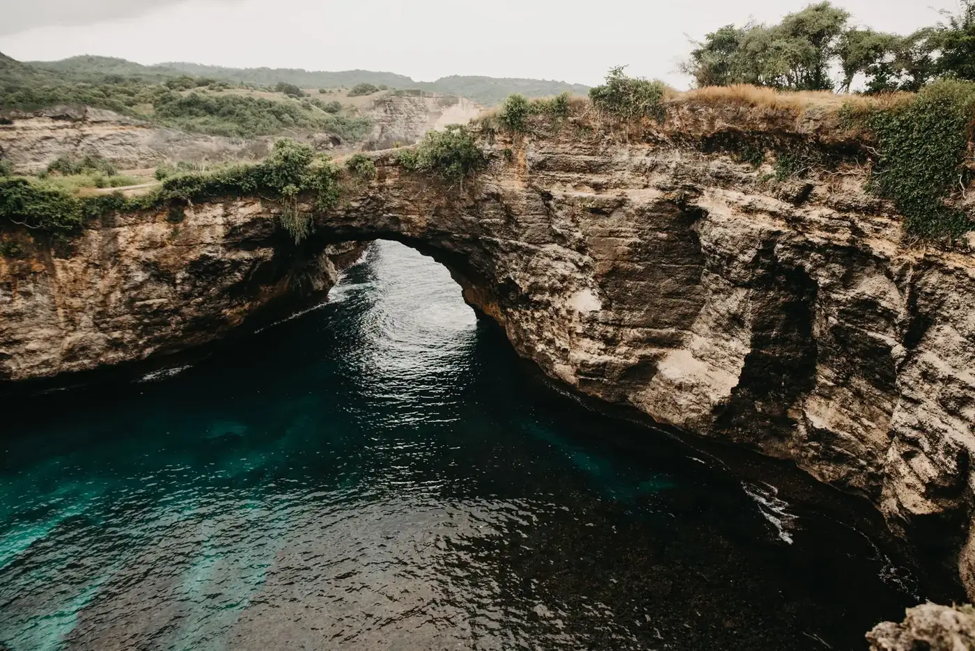 The Broken Beach arch and cove seen from the footpath on the rim, with the cliff dropping to the water