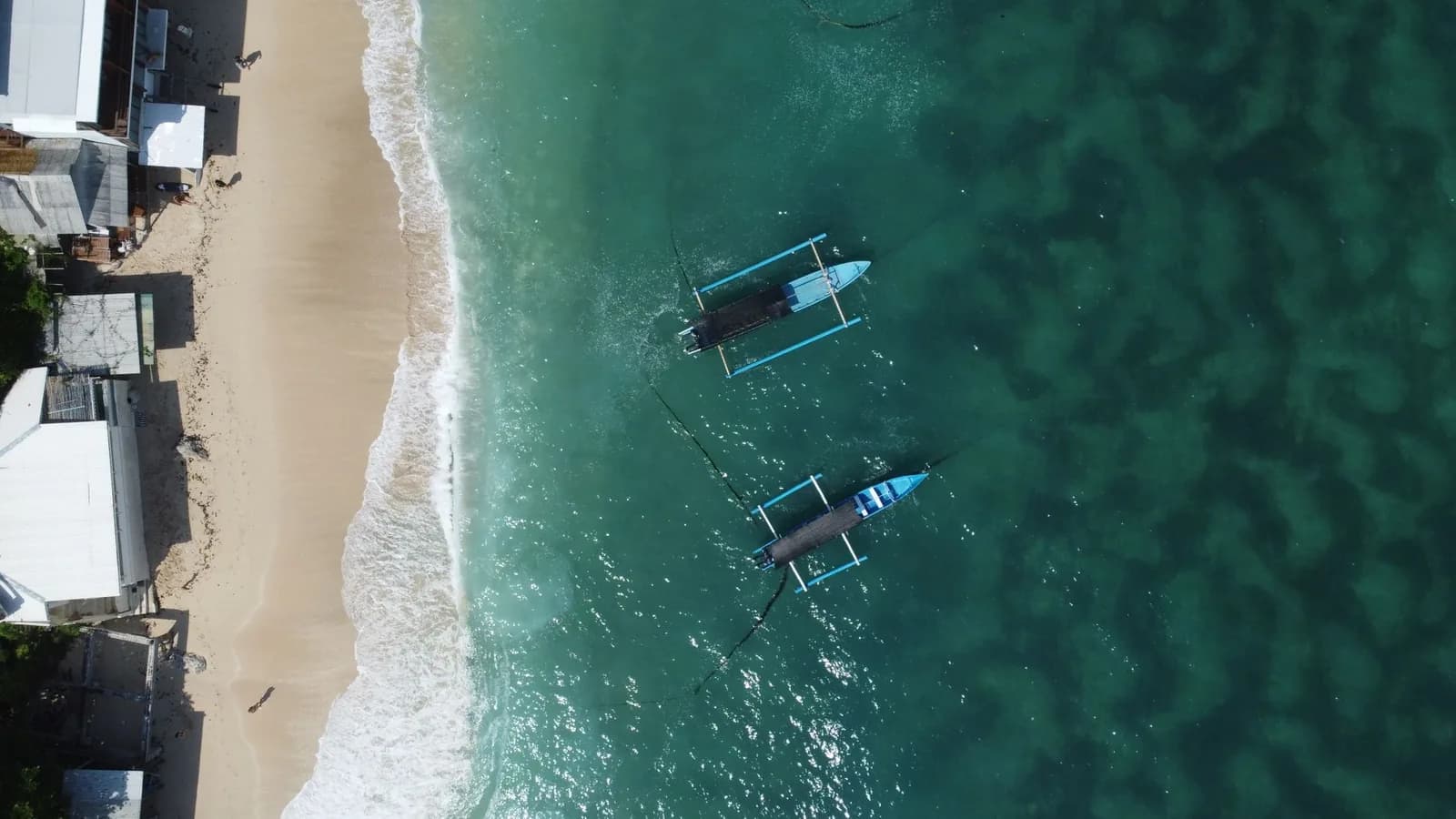 Outrigger boats moored over shallow reef off the beach at Crystal Bay, Nusa Penida, seen from above
