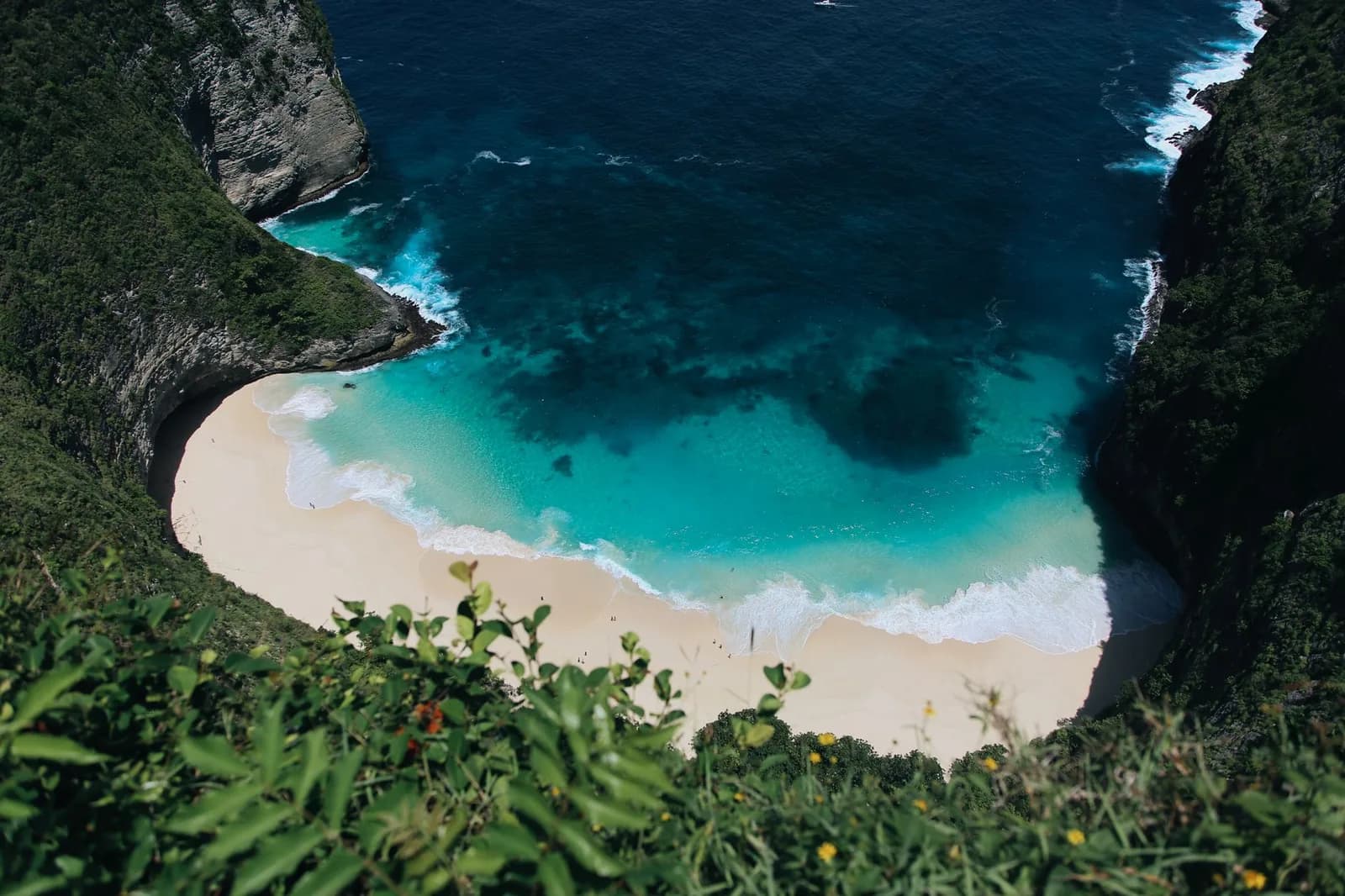Waves breaking the full length of the sand at Kelingking Beach, with people small on the shore, Nusa Penida