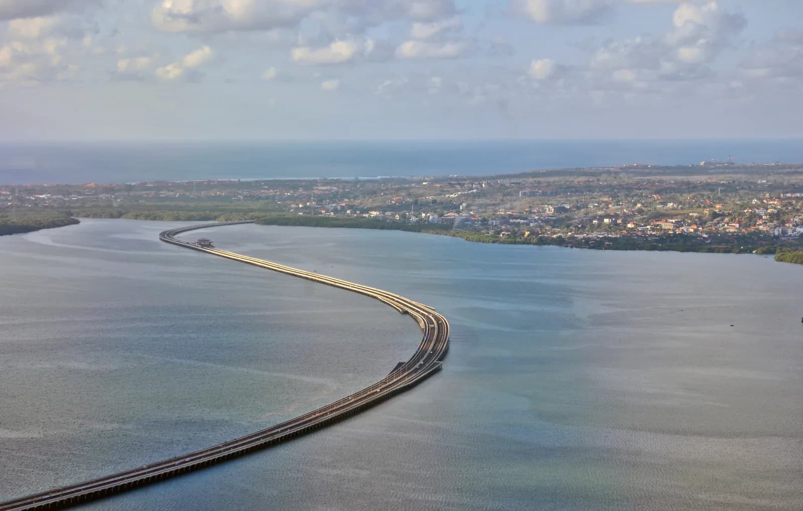 Aerial view of the Bali Mandara toll road curving over the water of Benoa Bay towards Nusa Dua