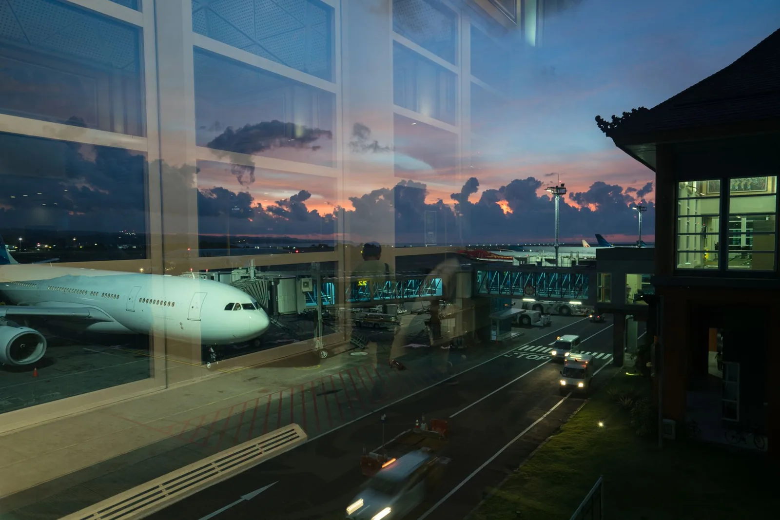 Aircraft parked at the gate at dusk, seen through the glass of the terminal in Bali