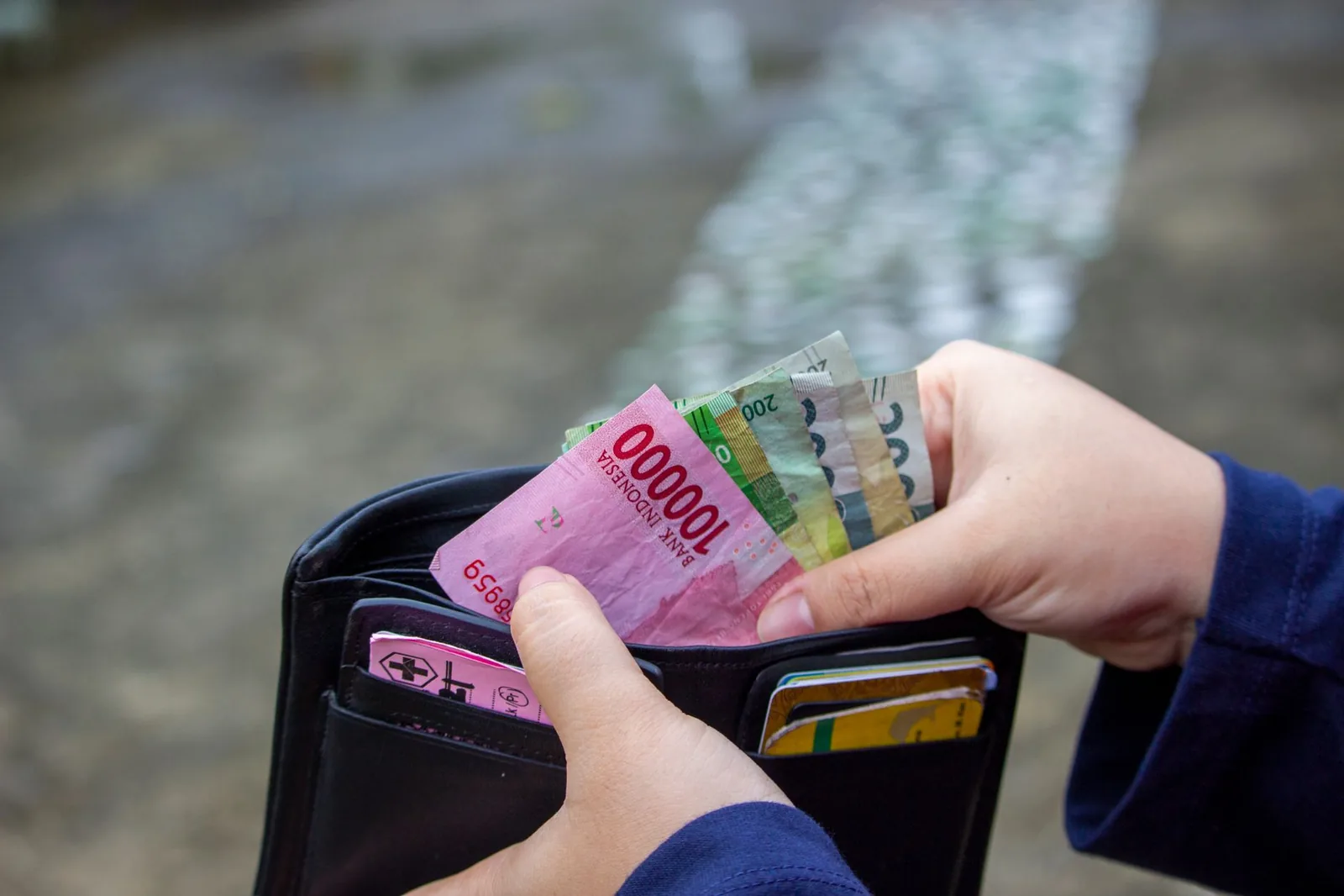 Hands pulling Indonesian rupiah banknotes, including a red 100,000 note, out of a wallet
