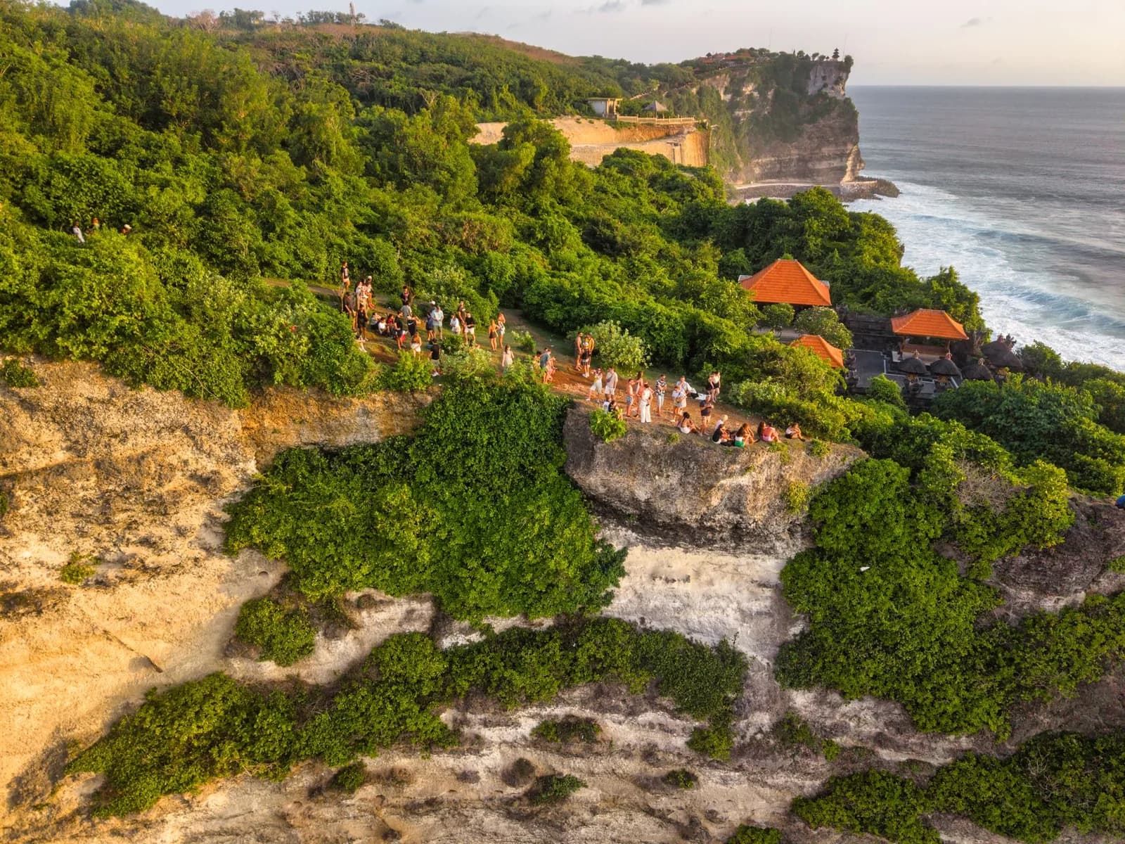 Line of visitors walking the clifftop path towards the shrines of Uluwatu temple above the sea, Bali