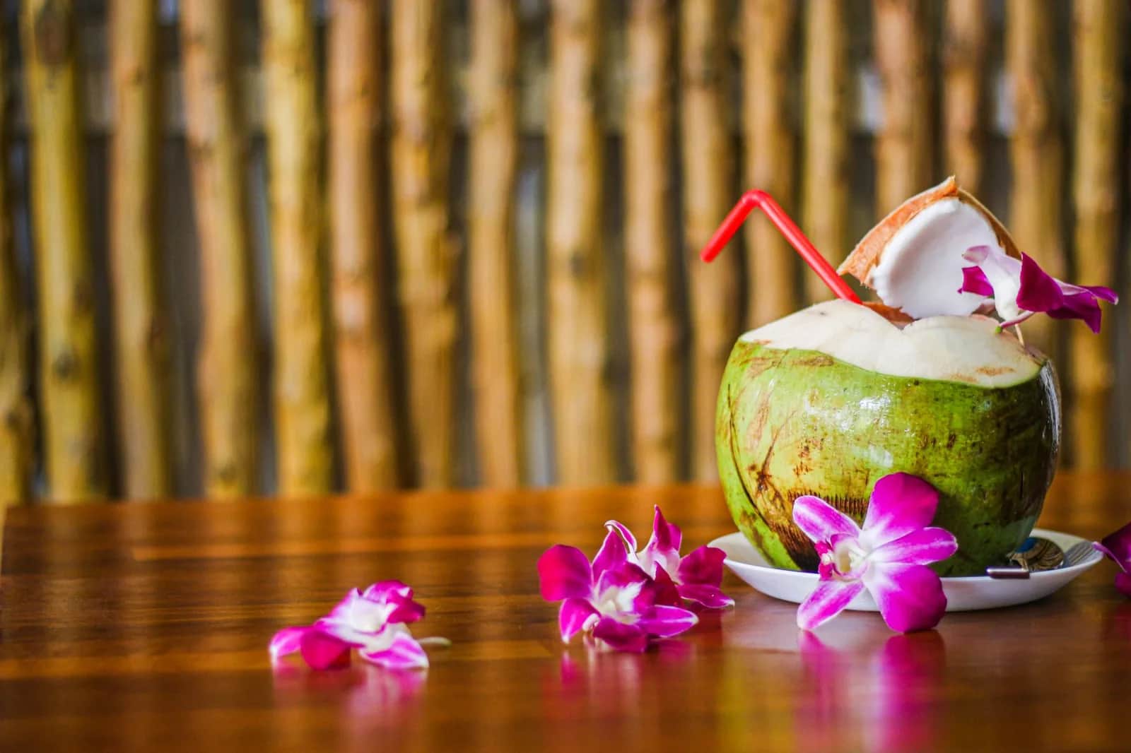 Fresh green coconut with a red straw and orchid flowers on a wooden table