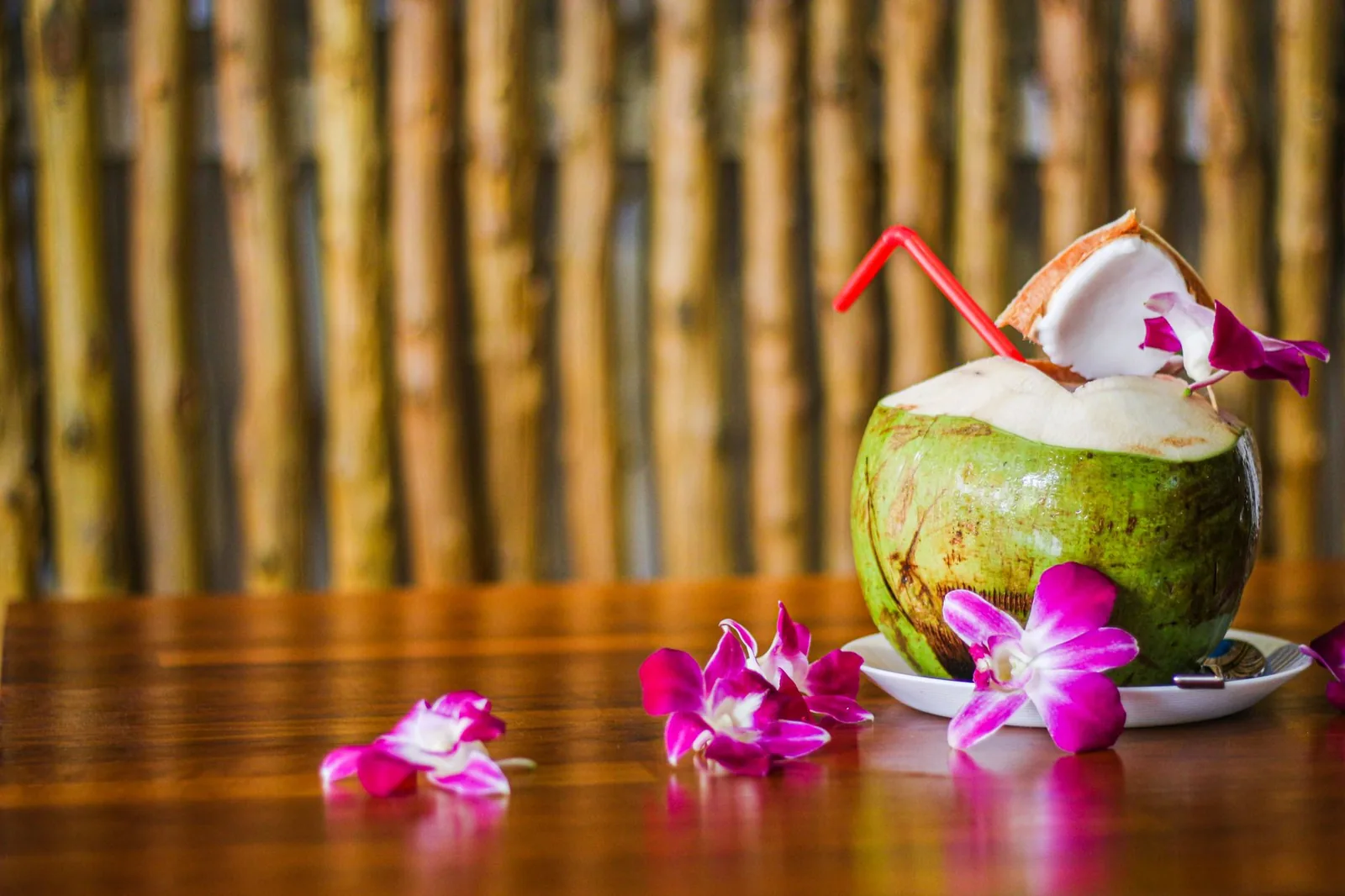 Fresh green coconut with a red straw and orchid flowers on a wooden table