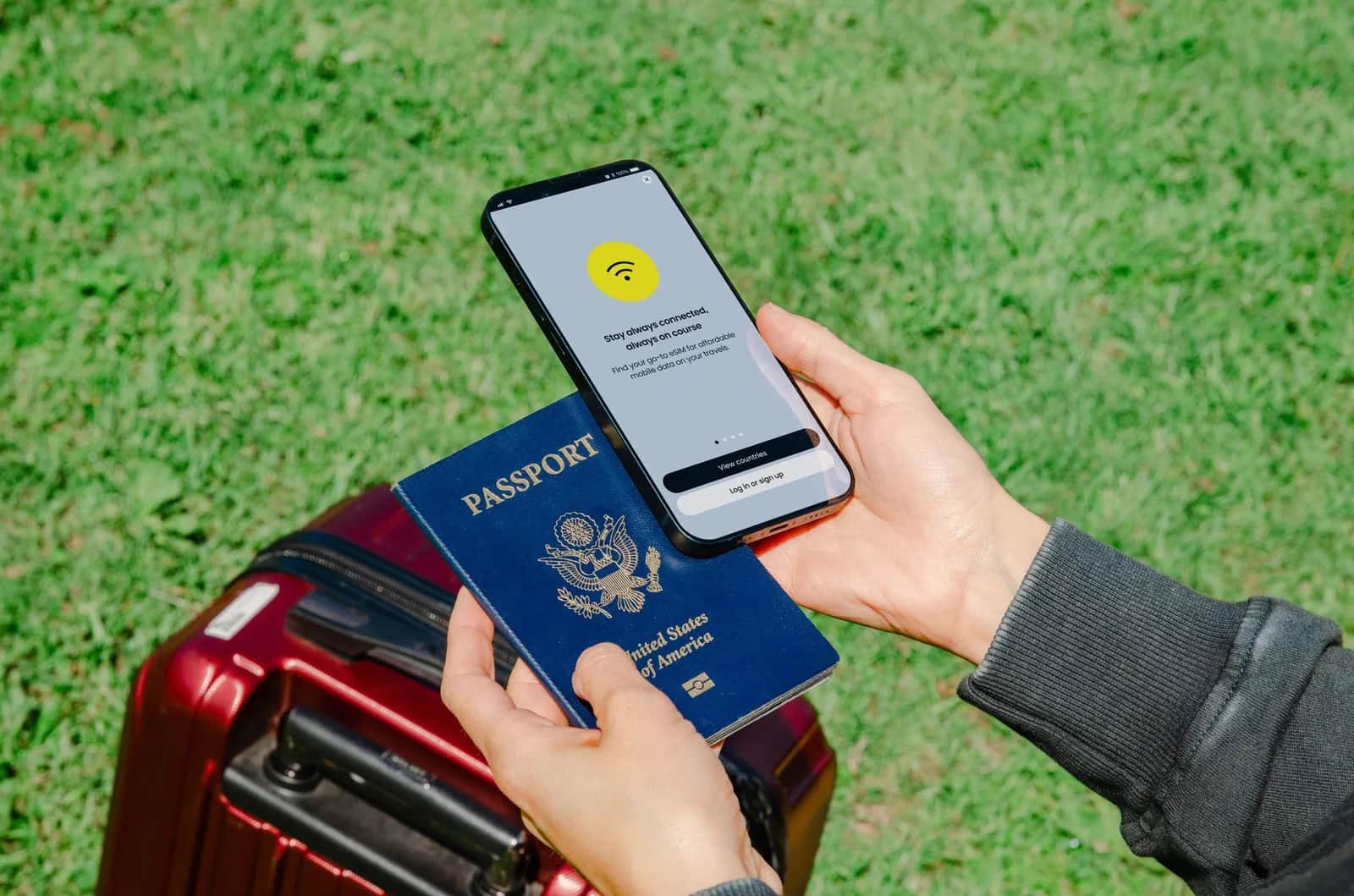 Traveller holding a passport and a smartphone next to a red suitcase