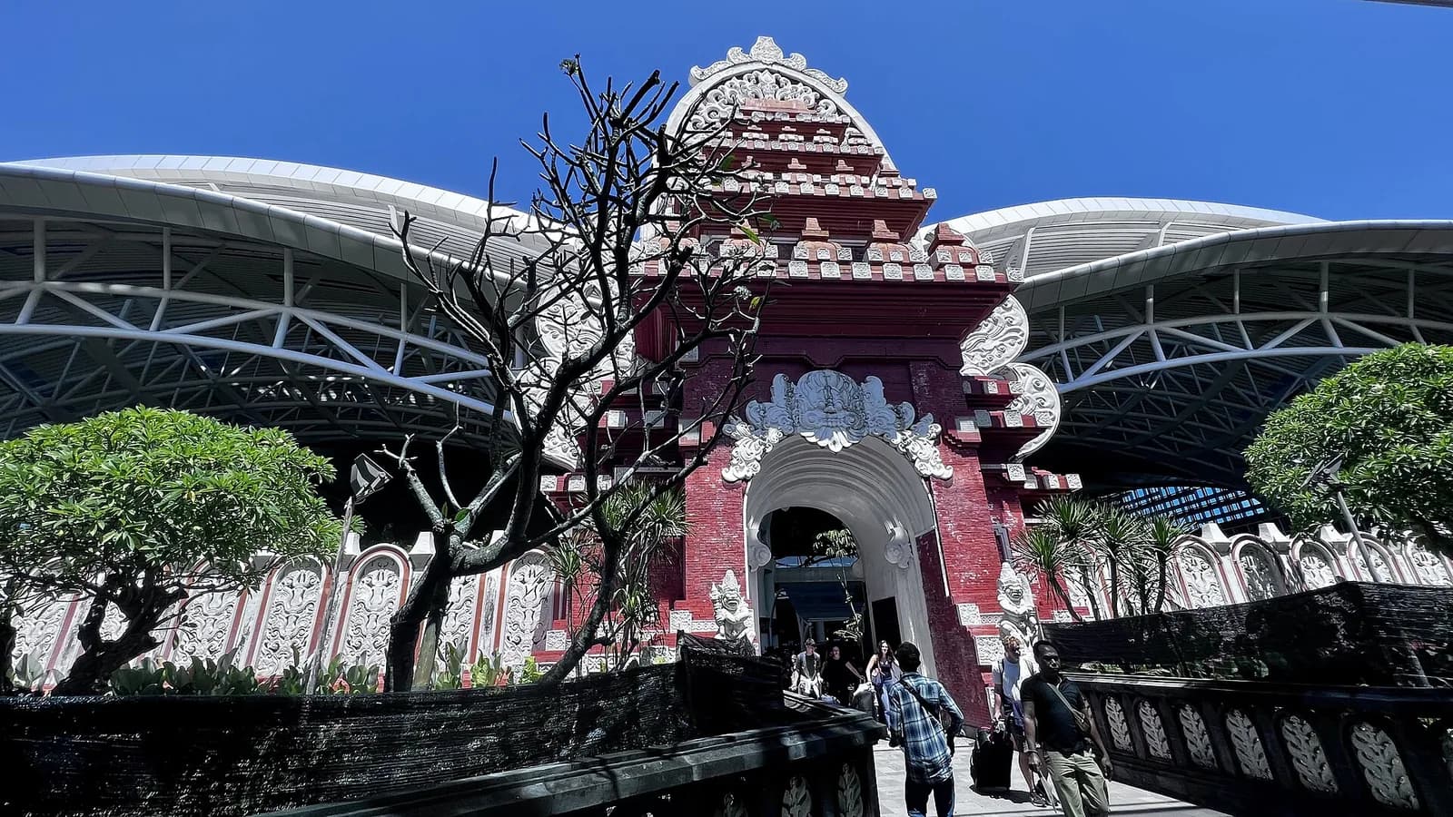 Carved red brick Balinese gate at the entrance to the international terminal of Ngurah Rai airport, Bali, with the curved steel roof behind