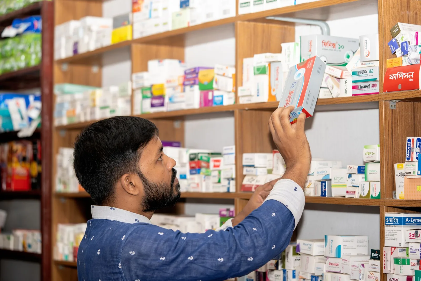 Pharmacist reaching for a box of medicine from well-stocked pharmacy shelves