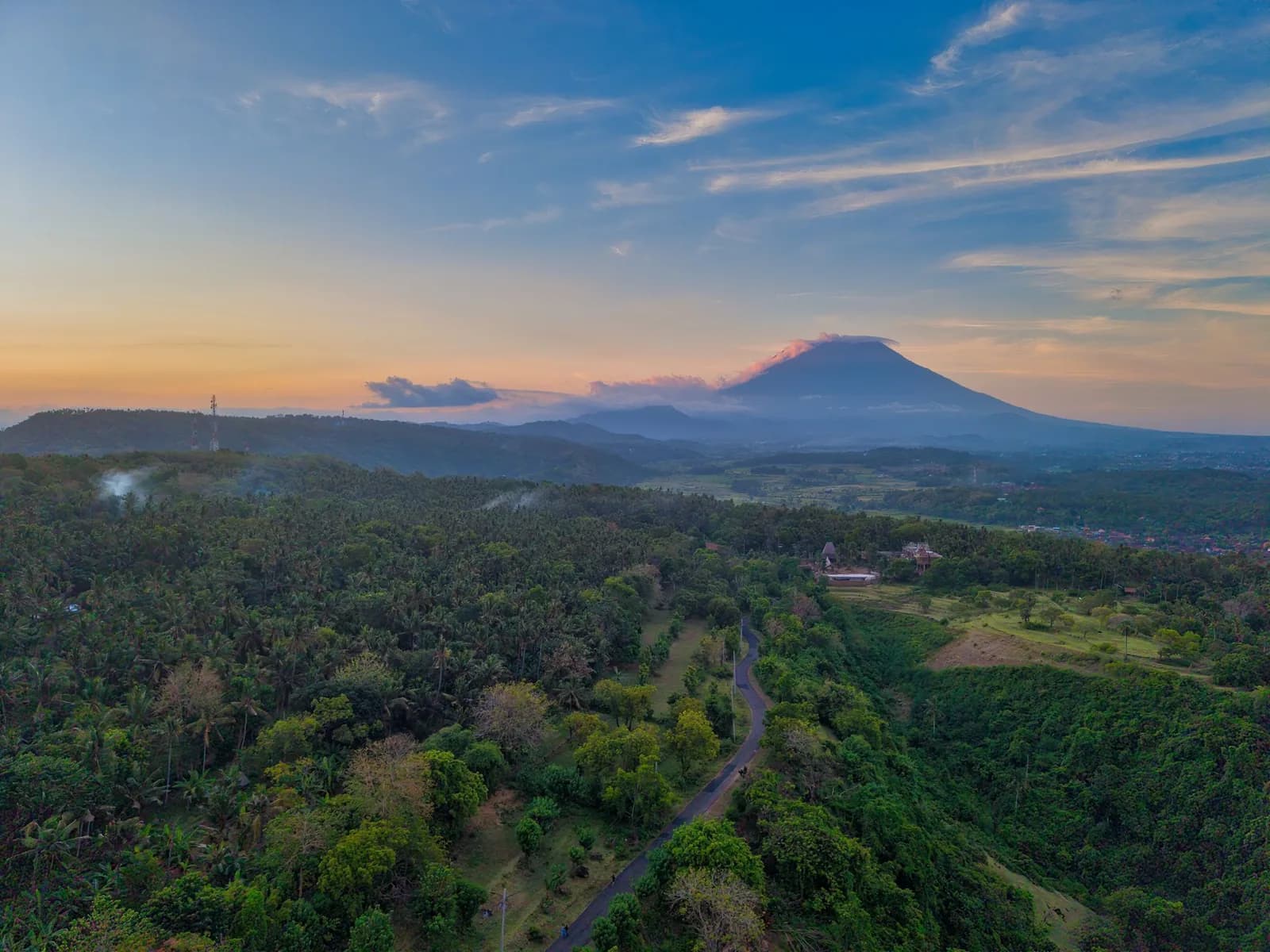 Narrow country road through coconut palms in eastern Bali with Mount Agung at sunset