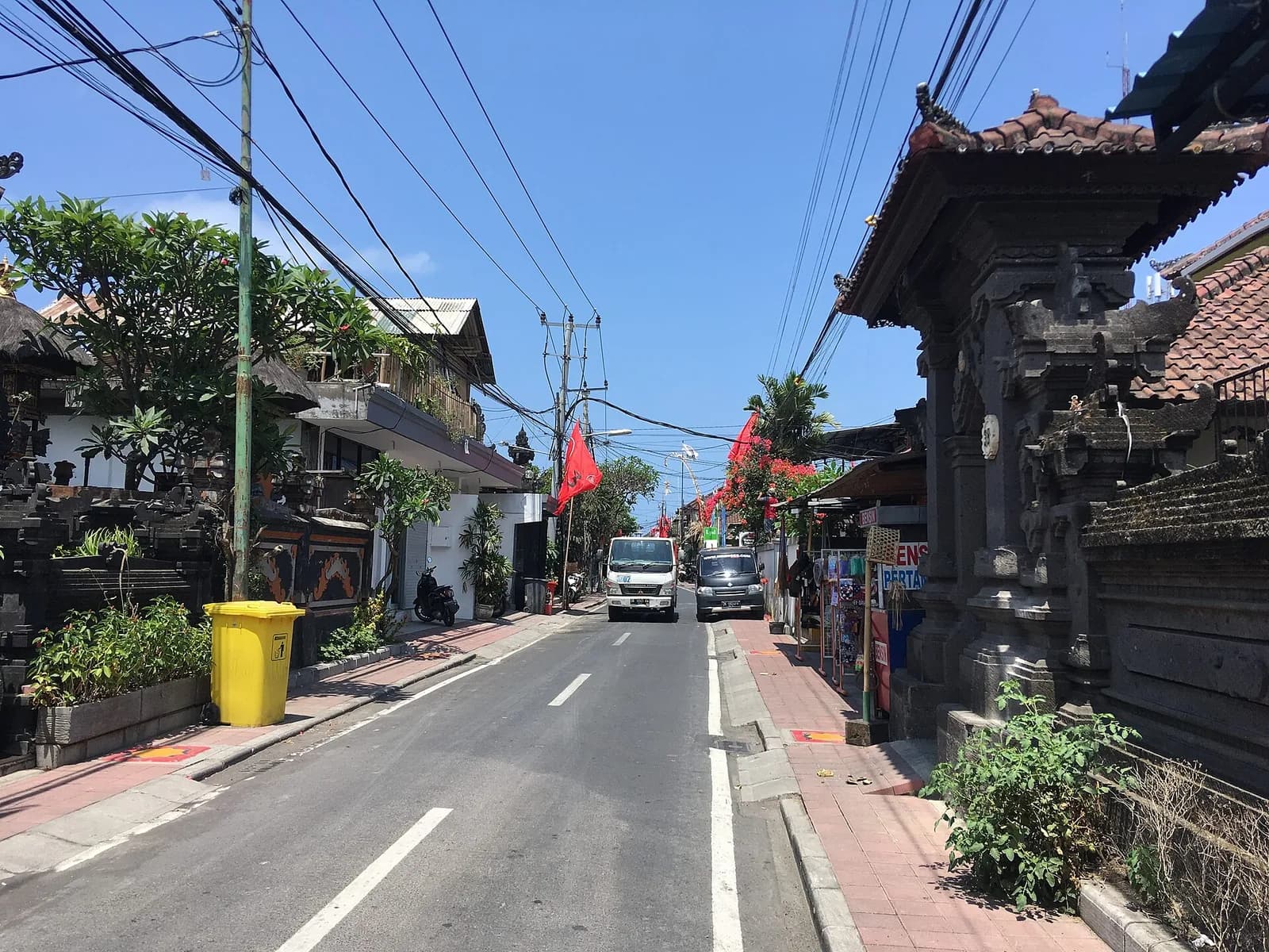 Street in Seminyak, Bali, with a Balinese temple gate and small shops along the road