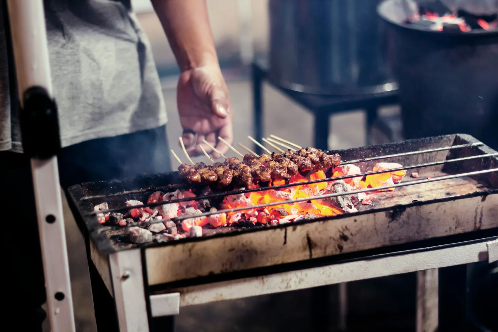 Street vendor grilling satay skewers over glowing charcoal at night