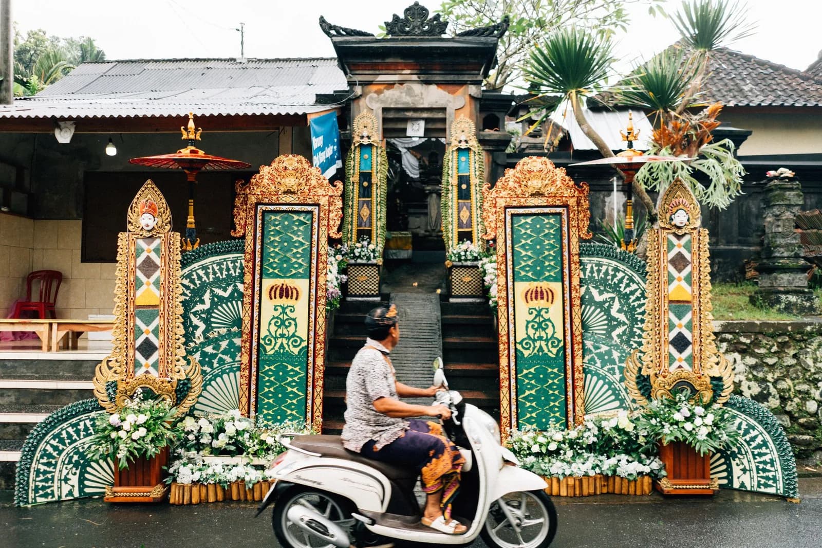 Scooter riding past an ornate Balinese gateway decorated for a ceremony, Bali