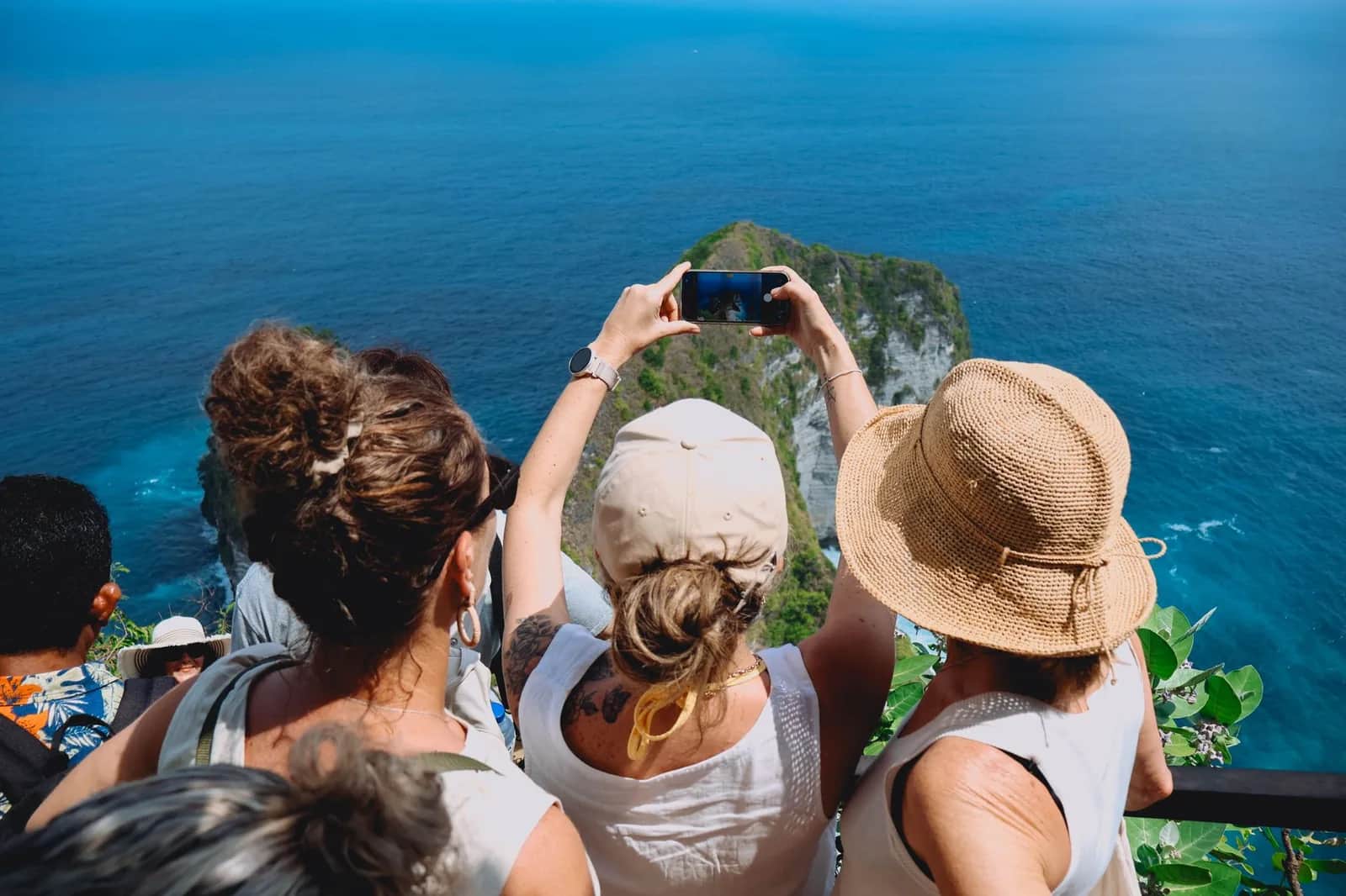 Travelers holding up a smartphone to photograph the sea from a tropical clifftop viewpoint
