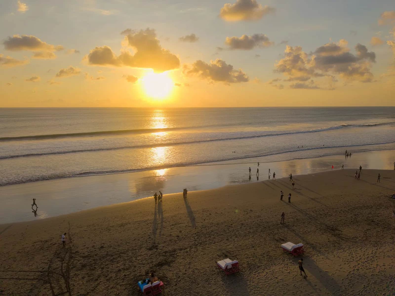 Sunbeds and umbrellas on the wide sand of Bali's west coast beach strip at sunset