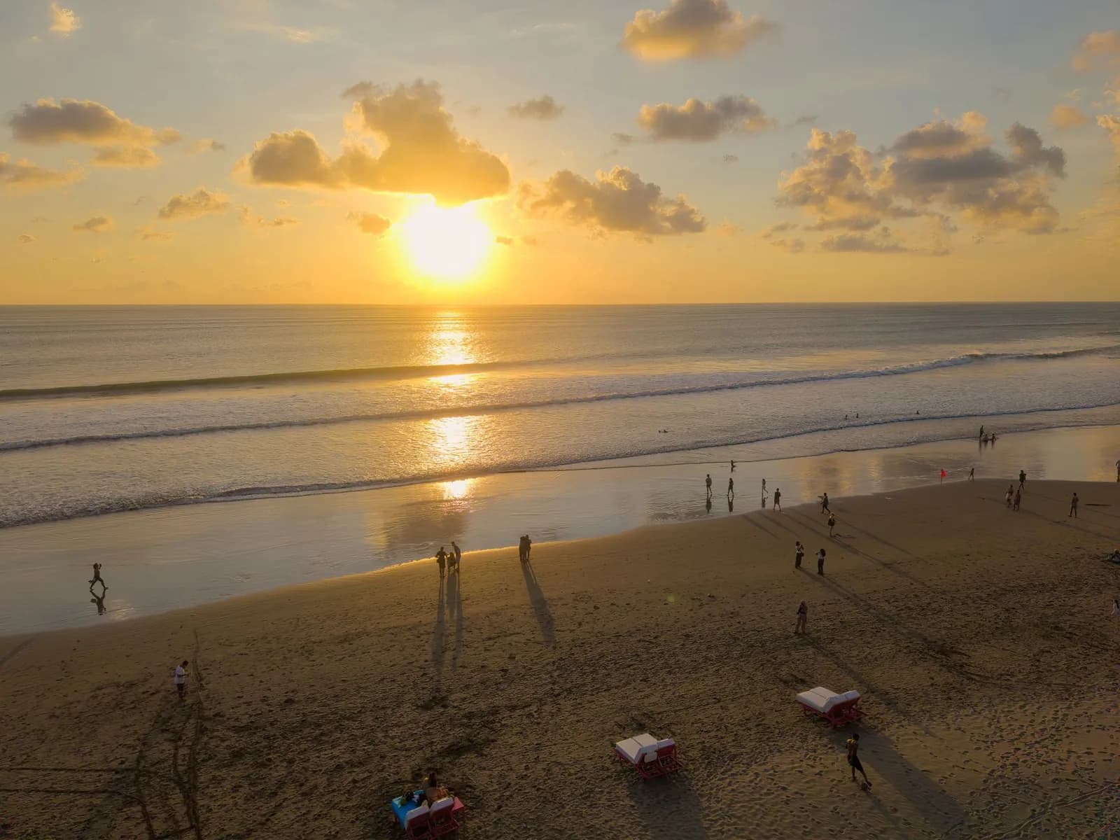 Sunbeds and umbrellas on the wide sand of Bali's west coast beach strip at sunset