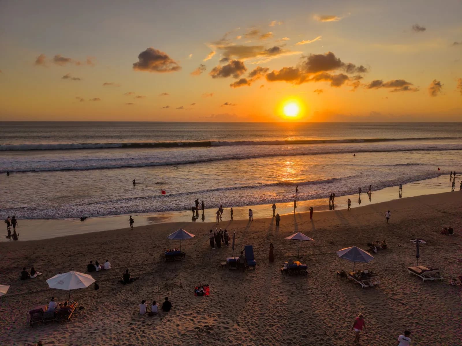 A red no swimming flag standing on the sand as the sun sets over the surf on Bali's west coast
