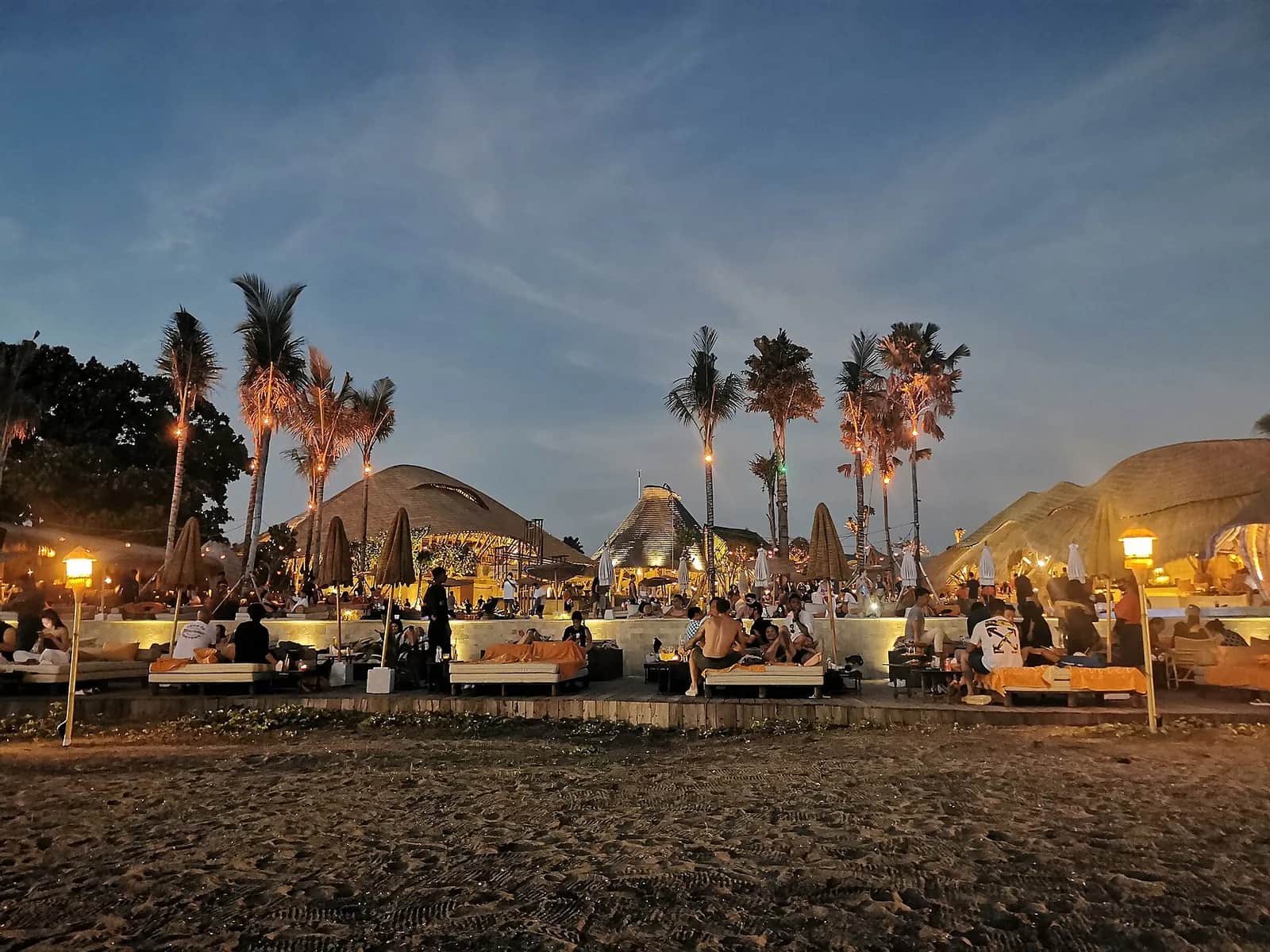 Mari Beach Club at dusk with daybeds, lanterns and thatched pavilions on the sand at Batu Belig, Bali