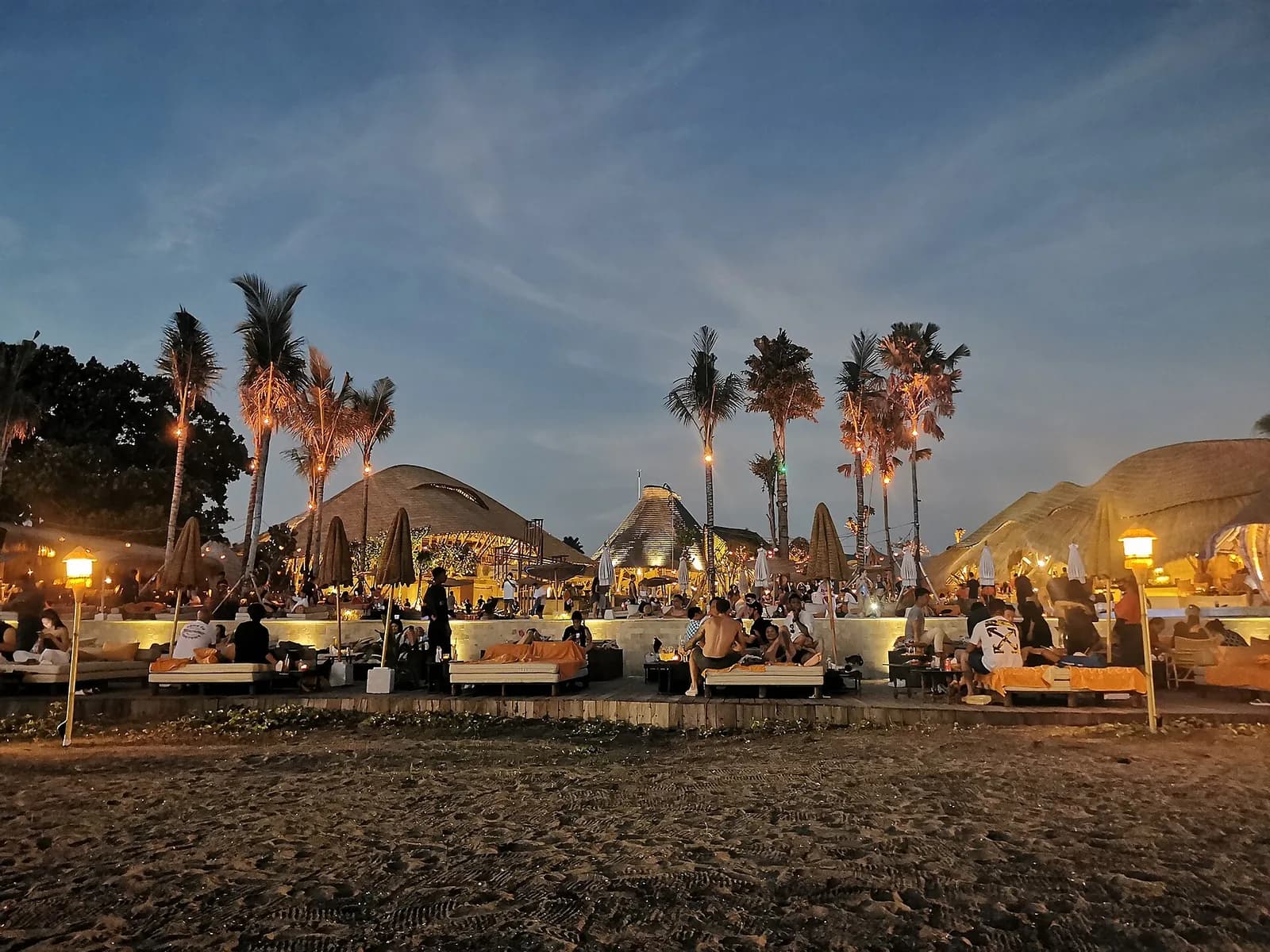 Mari Beach Club at dusk with daybeds, lanterns and thatched pavilions on the sand at Batu Belig, Bali