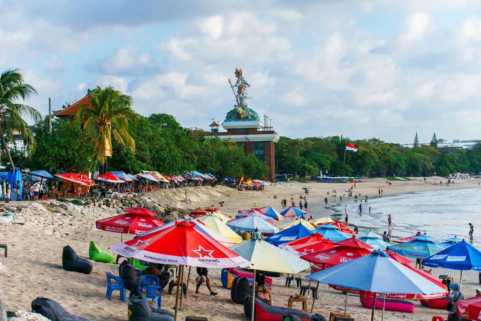 Rows of coloured umbrellas and beanbags on the crowded sand at Kuta beach, Bali