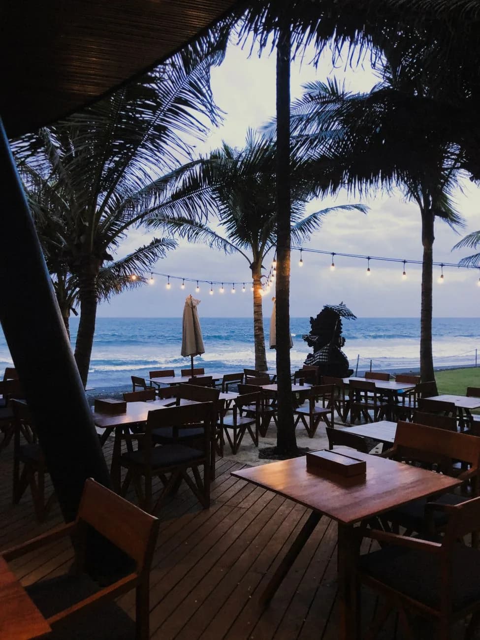 Beachfront tables and string lights facing the surf on Bali's west coast at dusk