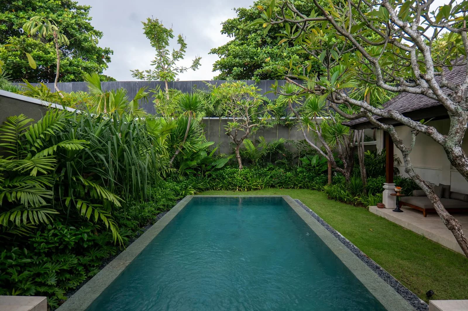 A private lap pool in the walled garden of a Balinese villa, with a frangipani tree and a thatched pavilion